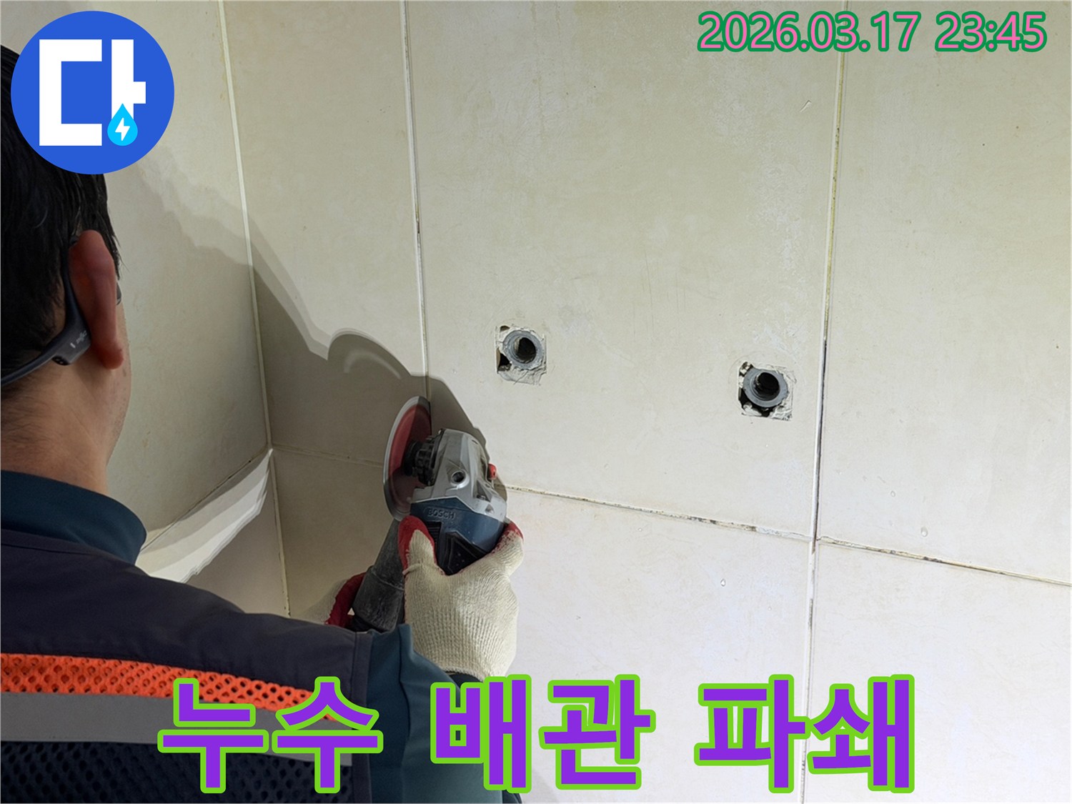 누수된 배관을-노출시키기 위해-전문가가-타일 벽면을-그라인더로-조심스럽게-파쇄하고-있습니다