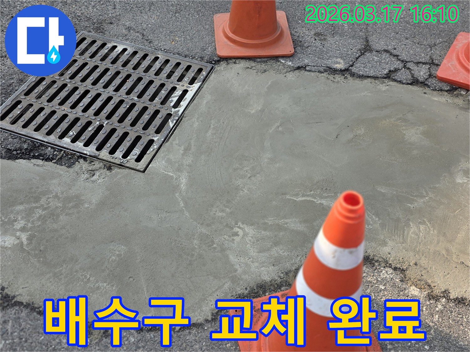 이 이미지는 양주 율정동의 외부 바닥 누수 문제로 인한 배수구 교체 작업이 완료된 상태를 보여주며-새로운 시멘트 마감과 안전 콘이 놓여 있습니다.