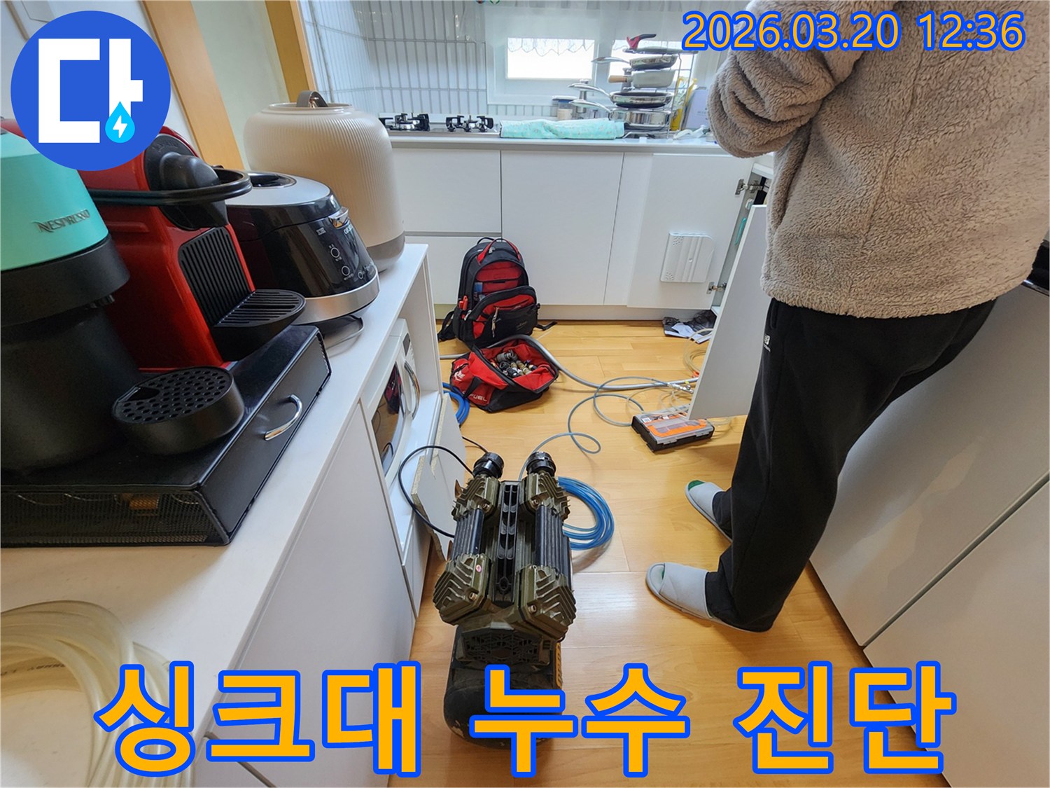 주방 싱크대 주변 바닥에 설치된-누수 진단 장비와-작업 준비 중인 전문가