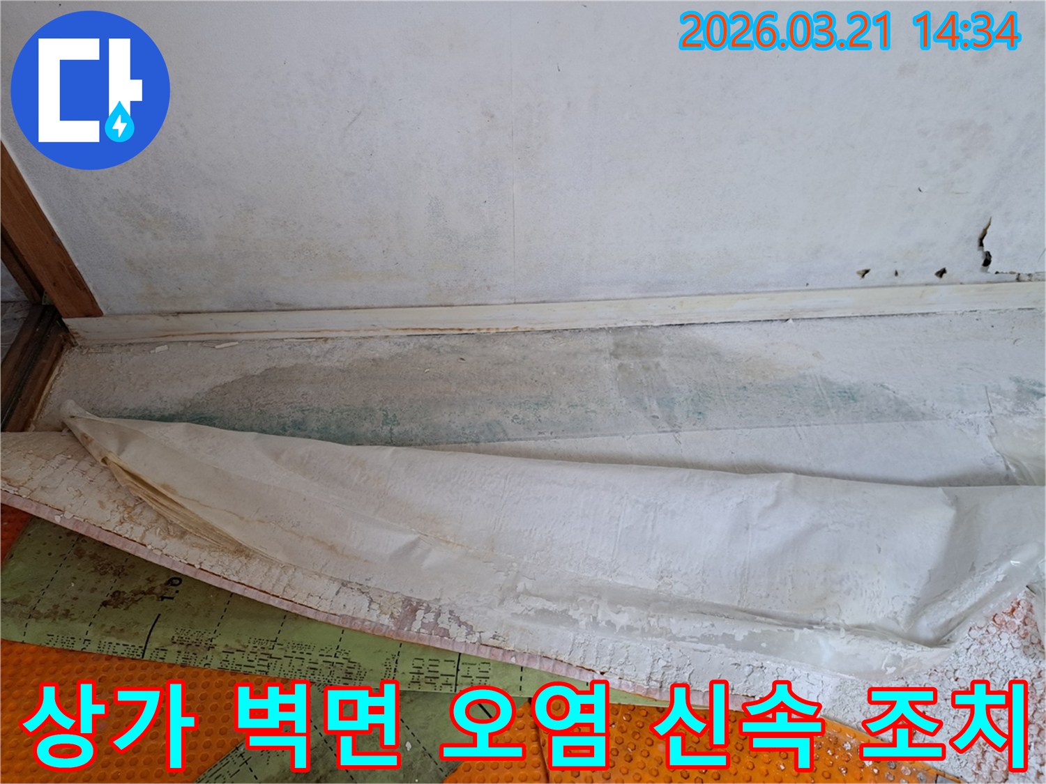 상가 벽면 하단의 오염과-바닥 보양재 아래의 습기를 통해-신속한 누수 조치가 필요한 현장을 보여주는 사진입니다.