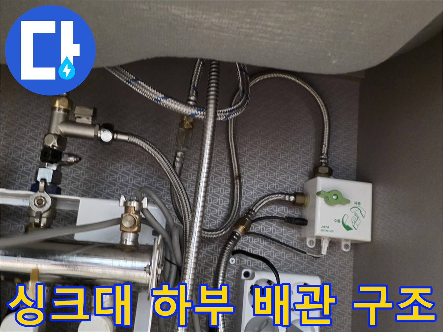 싱크대 밑 복잡한 수도 배관과 흰색 장치 및 콘센트 모습