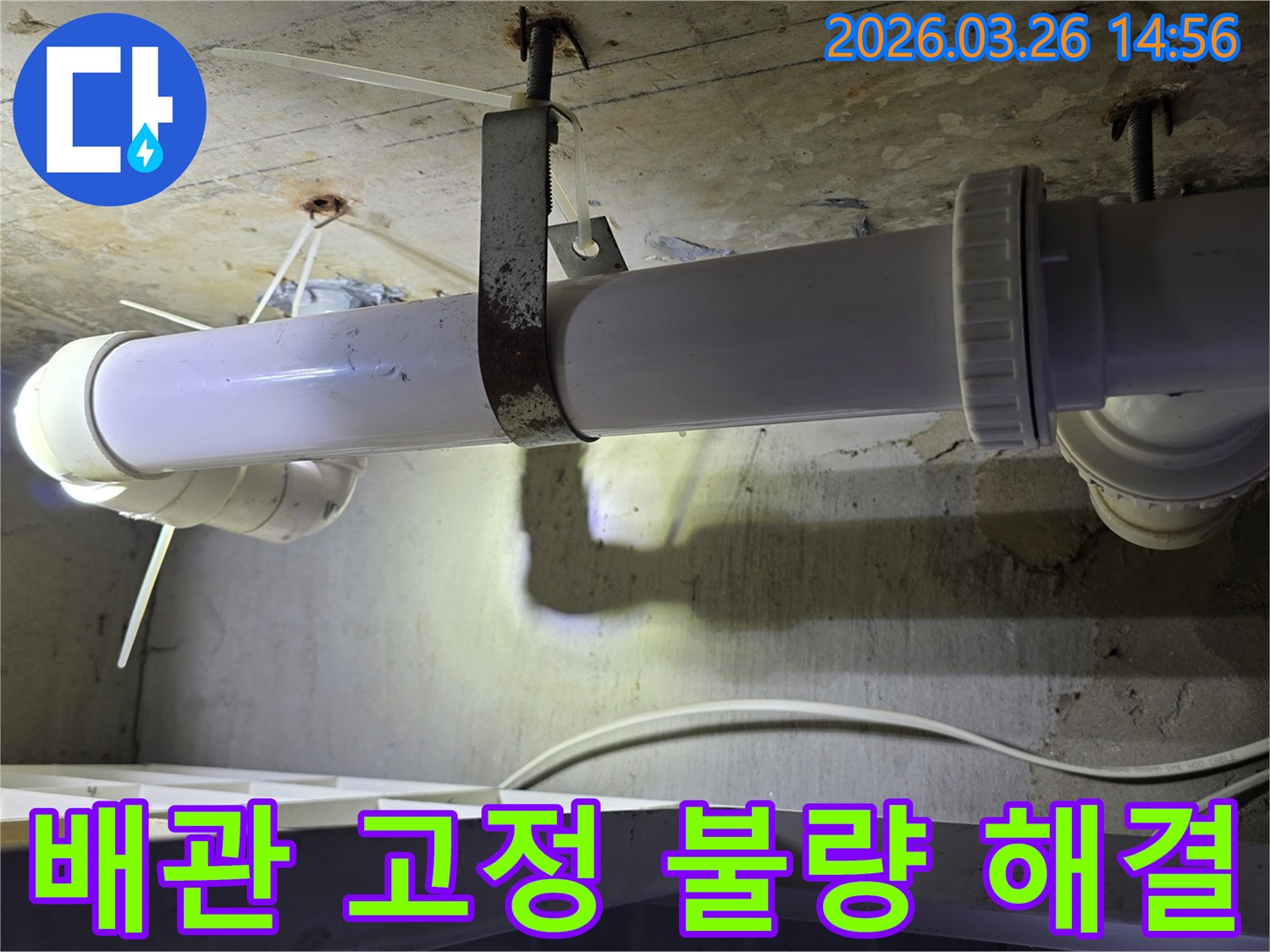 콘크리트 천장에 고정된-하얀색 배관과-오래되고 녹슨 금속 지지대의 상태를-엔지니어가 확인하는 모습