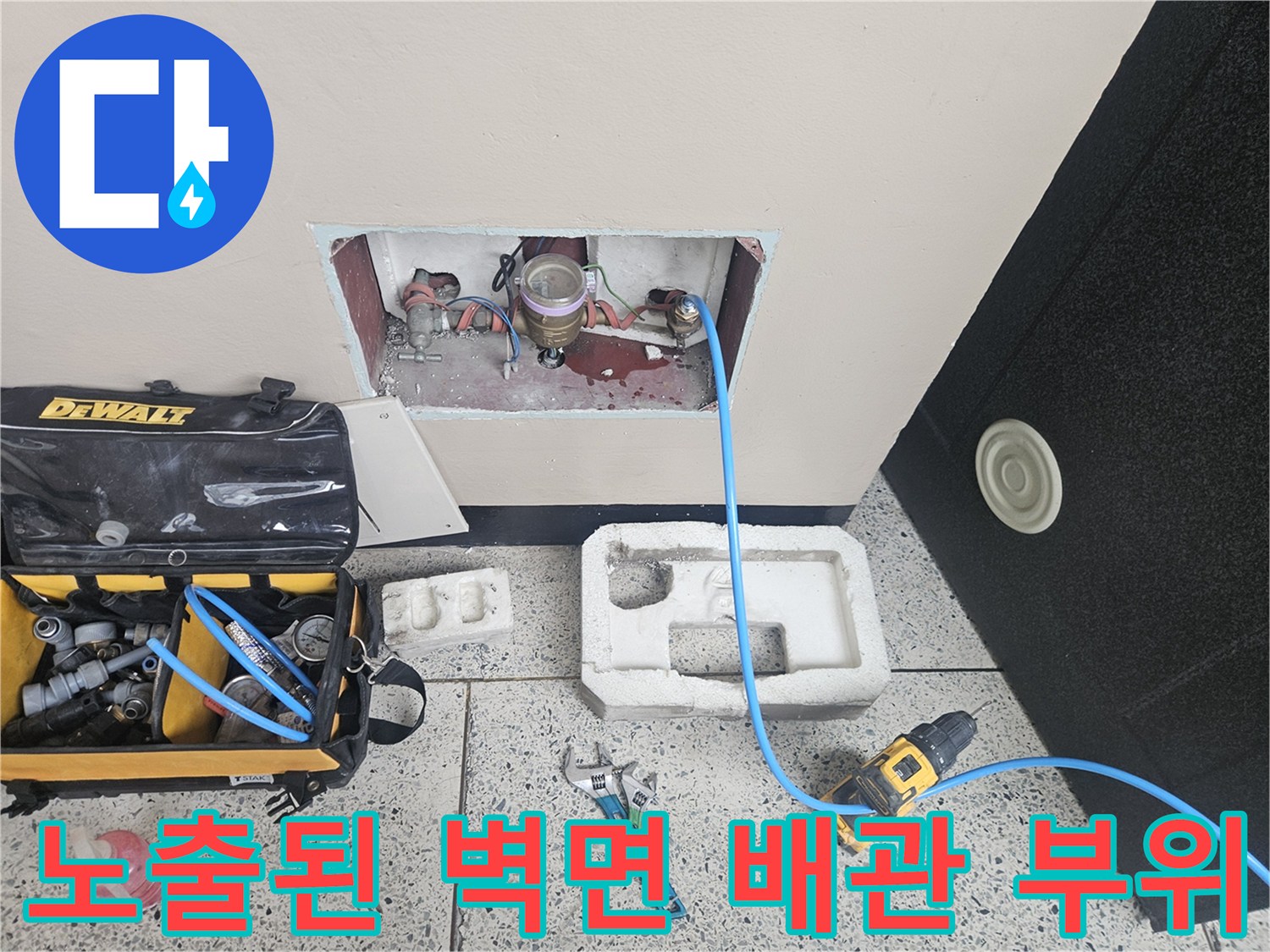 벽 내부의 노출된 수도 배관과 주변 작업 공구들