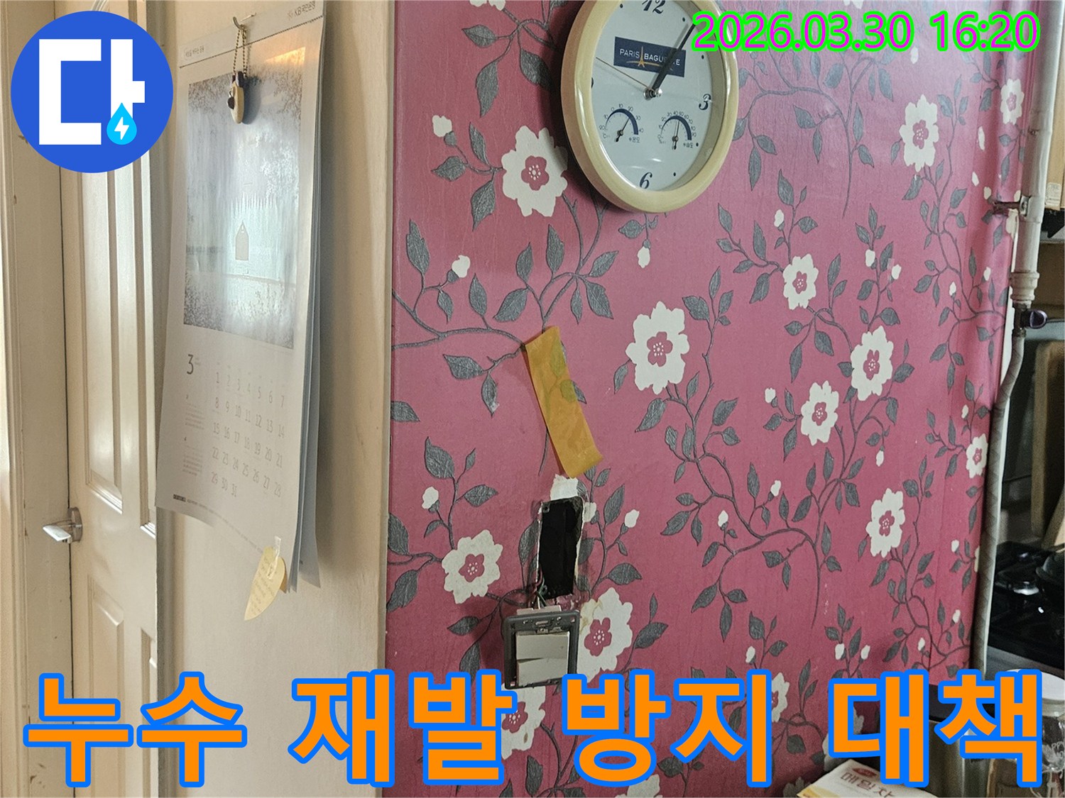 분홍색 꽃무늬 벽지에-시계가-걸려있고-누수-탐지를-위해-개방된-벽면을-보며-누수-재발-방지-대책을-설명하는-사진입니다