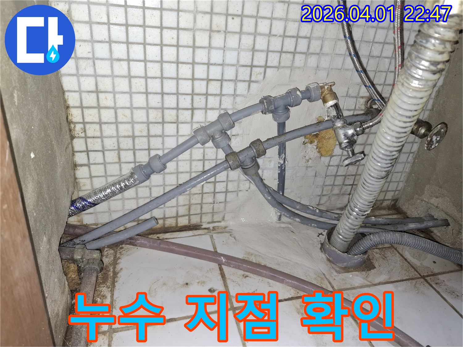 복잡하게 연결된-회색 배관들 사이에서-물이 새어 나와-바닥에 고여있는-누수 현장을-상세히 보여주는-이미지입니다.