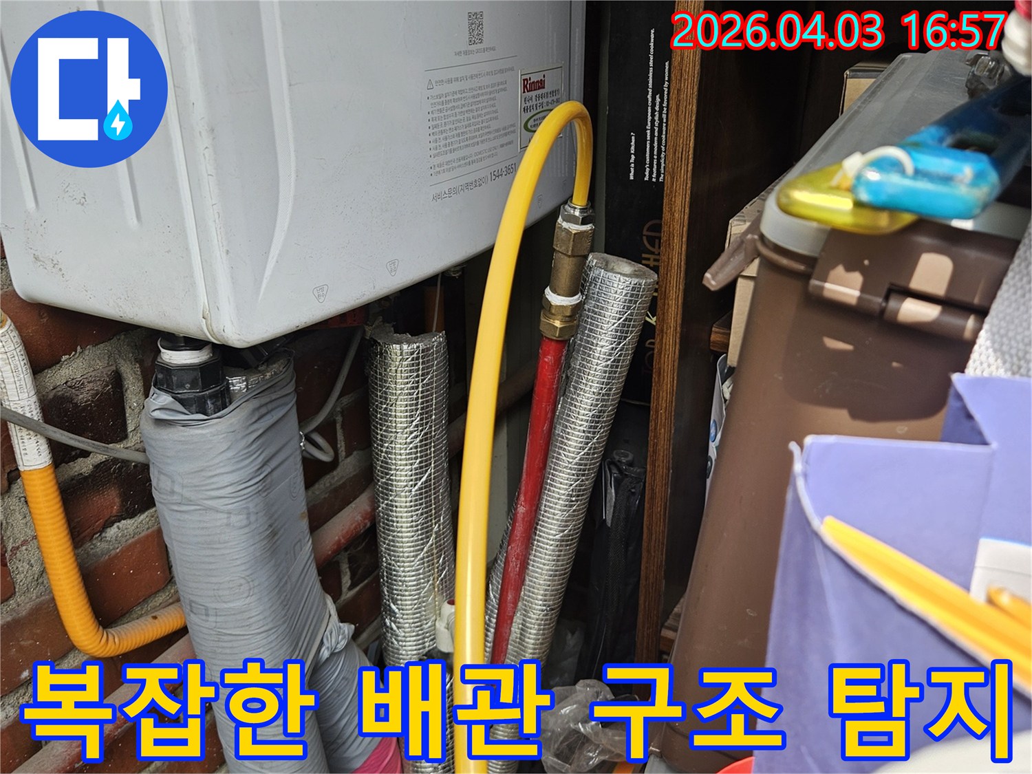 누수 탐지 전문가가 현장을 방문하여 보일러 하단의 배관들을 면밀히 검토하고 있는 장면입니다-파손된 단열재와 배관의 상태를 확인 중입니다.