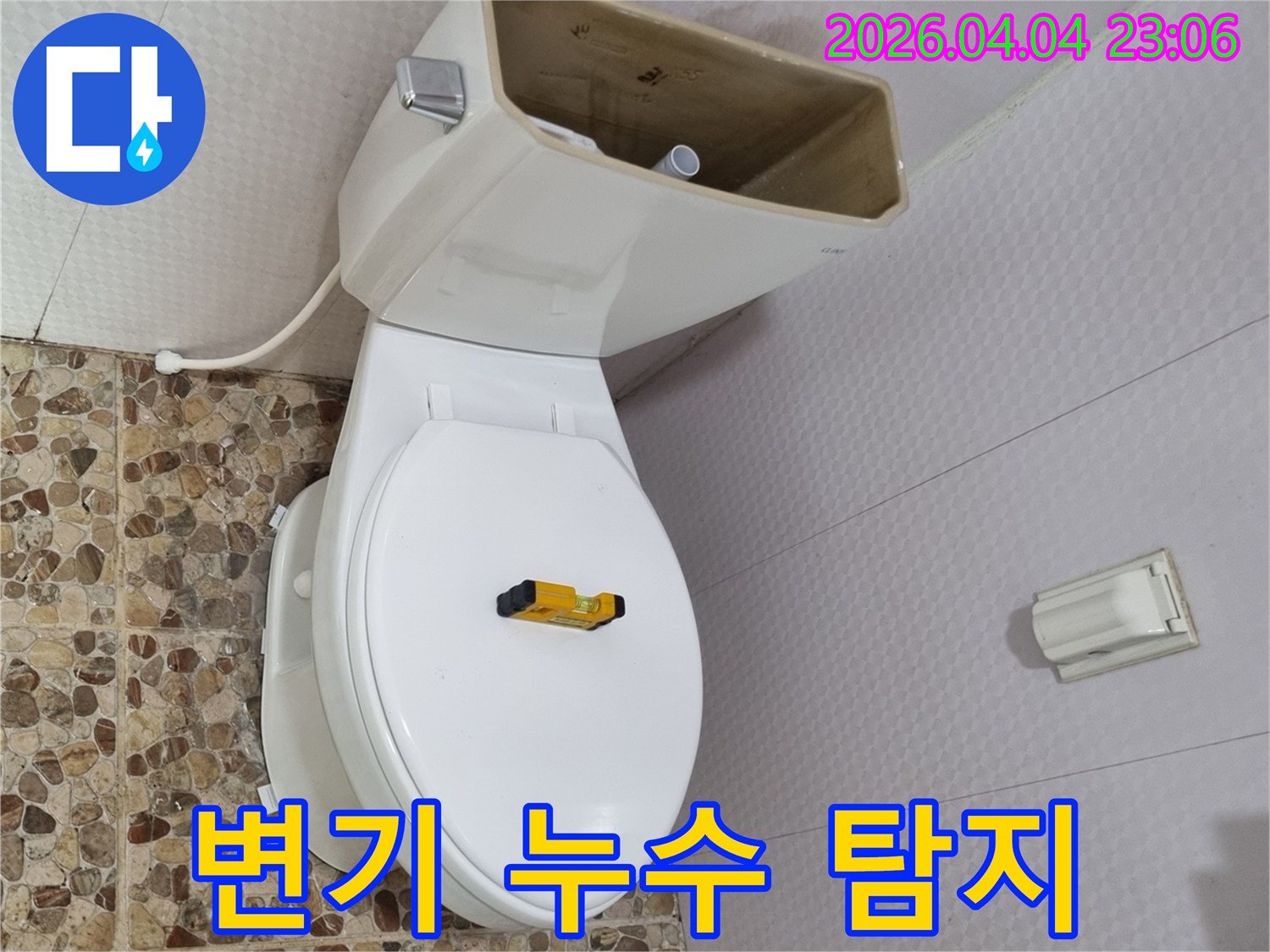 변기 물탱크가 열려 내부 부품이 노출된 상태로-수평계가 변기 시트 위에 놓여-누수 탐지 작업이 진행되고 있습니다