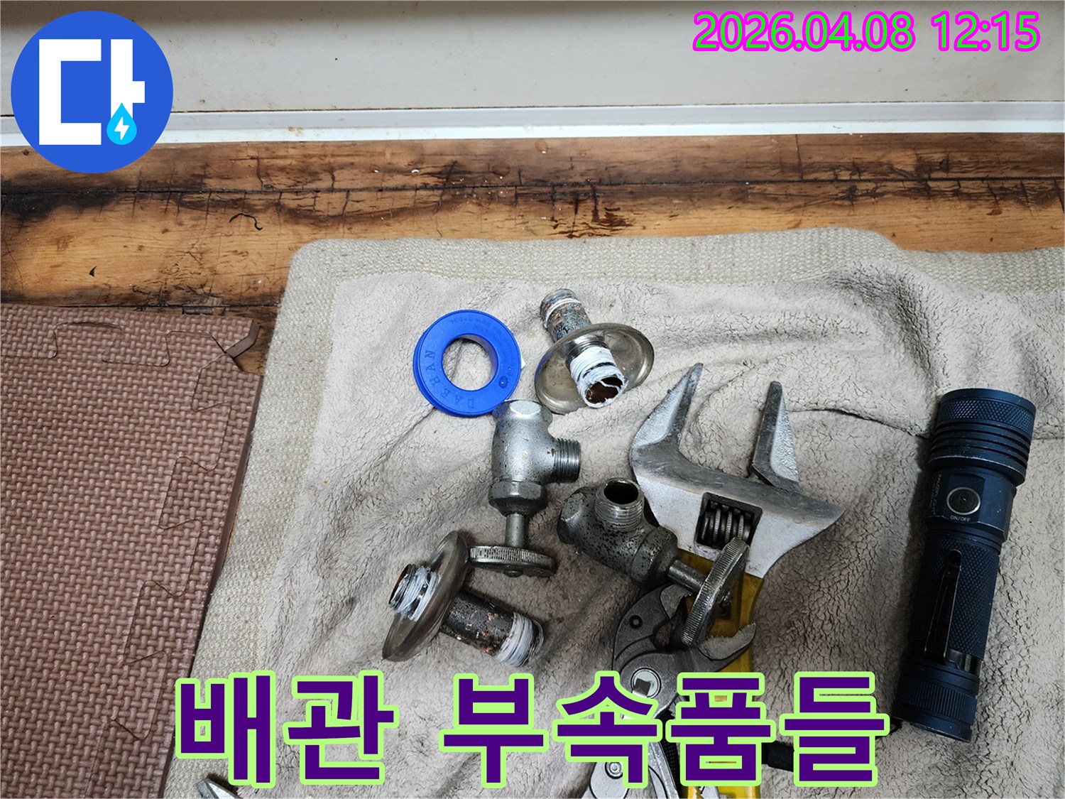 누수 공사 현장에서-교체될 배관 부속품들과-필수 공구들이-수건 위에 가지런히 놓여있습니다