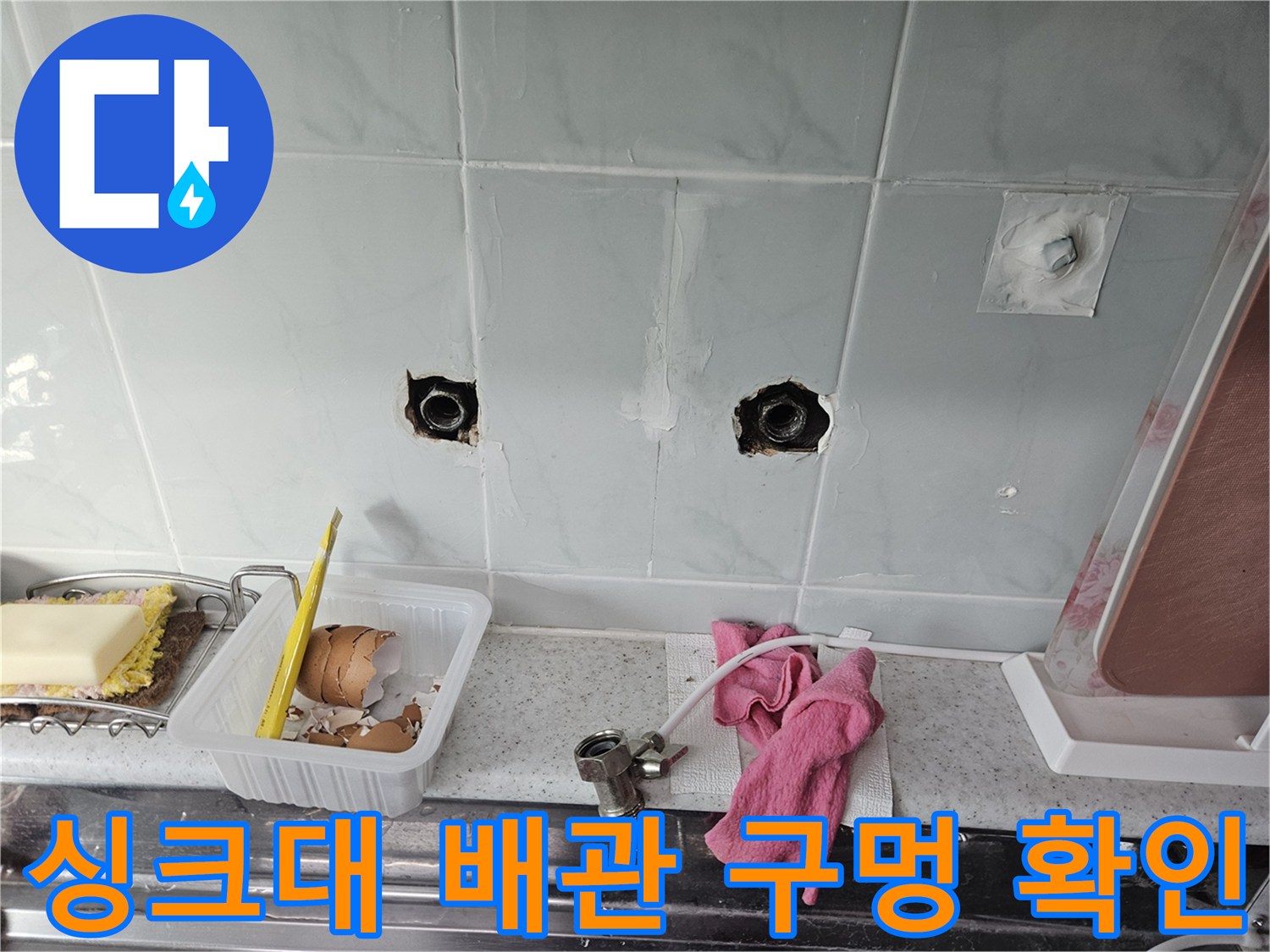 싱크대 하부 벽면 타일에 노출된 배관 연결 부위 모습