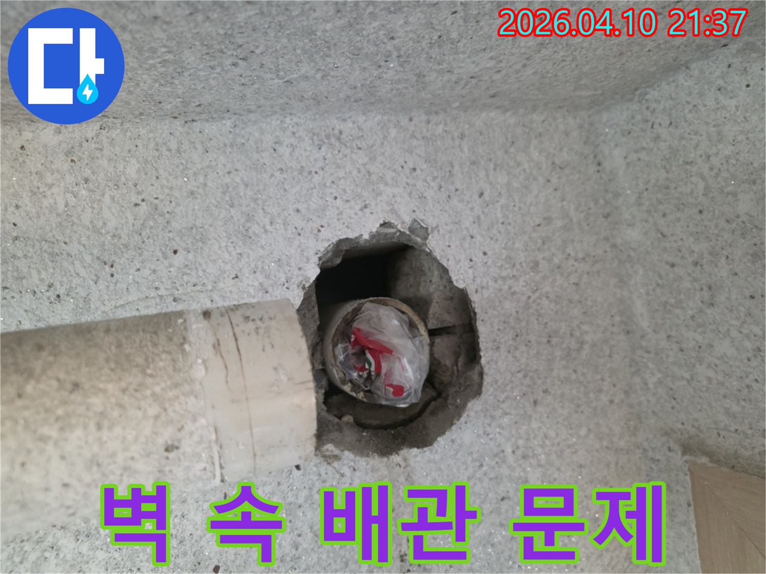 콘크리트 벽면의-파손된 구멍으로-보이는-배관 내부의-이물질과-임시 마감 상태를-보여주는-사진입니다