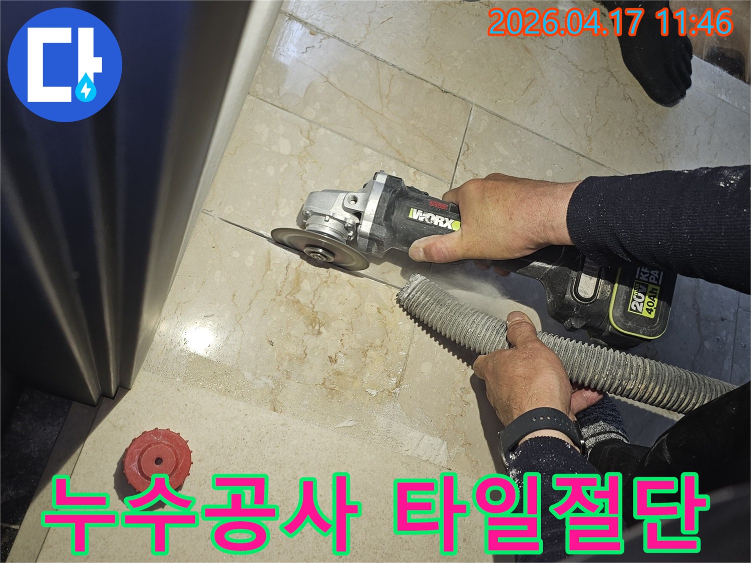 누수공사 시작을 위해 작업자가 그라인더로 바닥 타일을 절단하고-있으며-동시에-흡진기로-먼지를-제거하여-깨끗한-작업-환경을-조성하는-모습입니다.