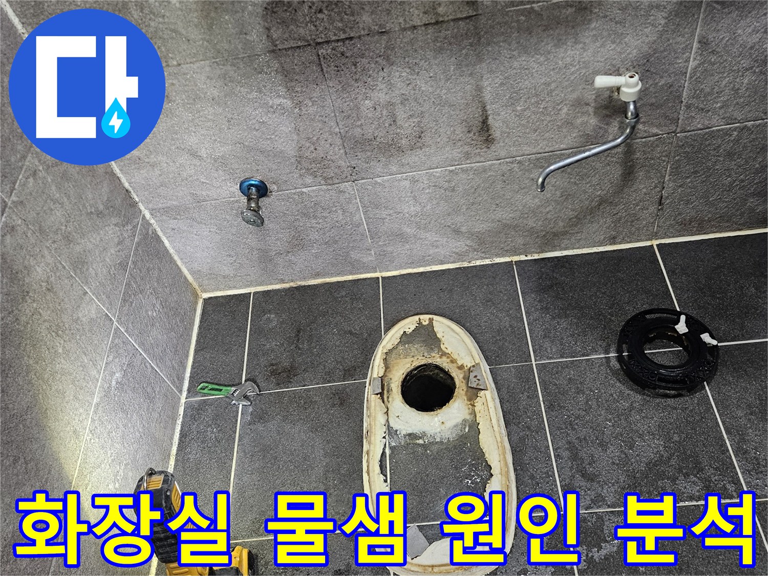 변기가 제거된 화장실 바닥의 배수구와-주변 타일에 스며든 물의 흔적을-손전등으로 밝혀 물샘 원인을 분석하는 작업 현장입니다.