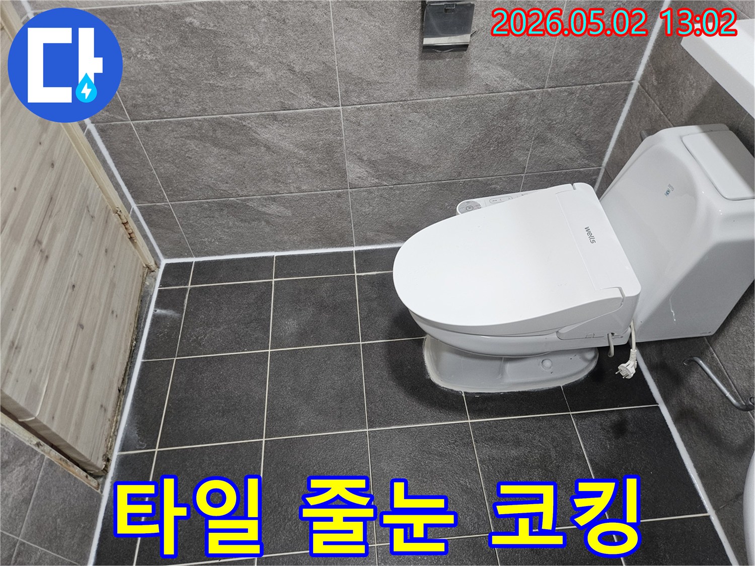 이 이미지는 욕실 바닥과 벽 타일의 줄눈-그리고 변기 주변에 새로 시공된 깨끗한 실리콘 코킹 마감 상태를 보여줍니다.