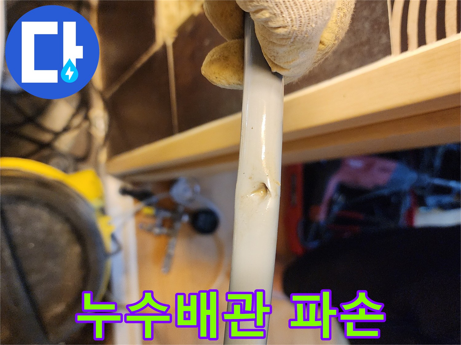 작업용 장갑을 낀 손이-누수 원인으로 보이는-손상된 배관의-구멍을 가리키고 있는-현장 사진입니다.