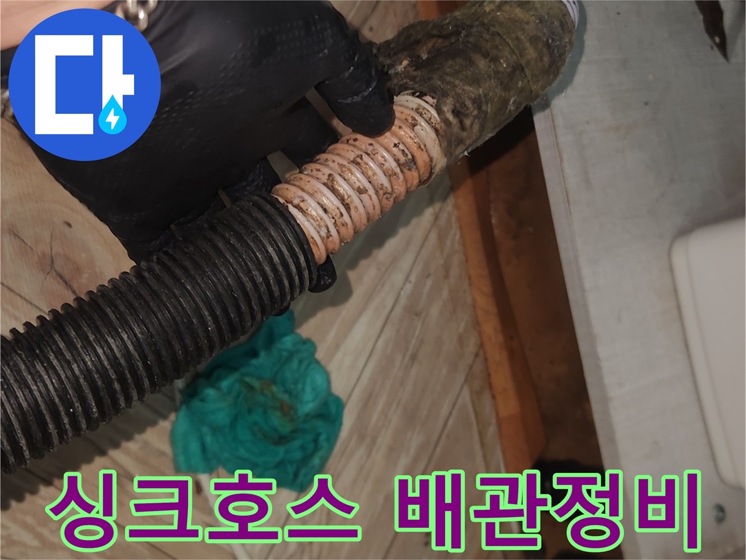 검은 장갑을 낀 손이-오랜 사용으로 오염된 싱크대 배수 호스를-들어 올린 채-석션 클리닝을 시작하려는 장면