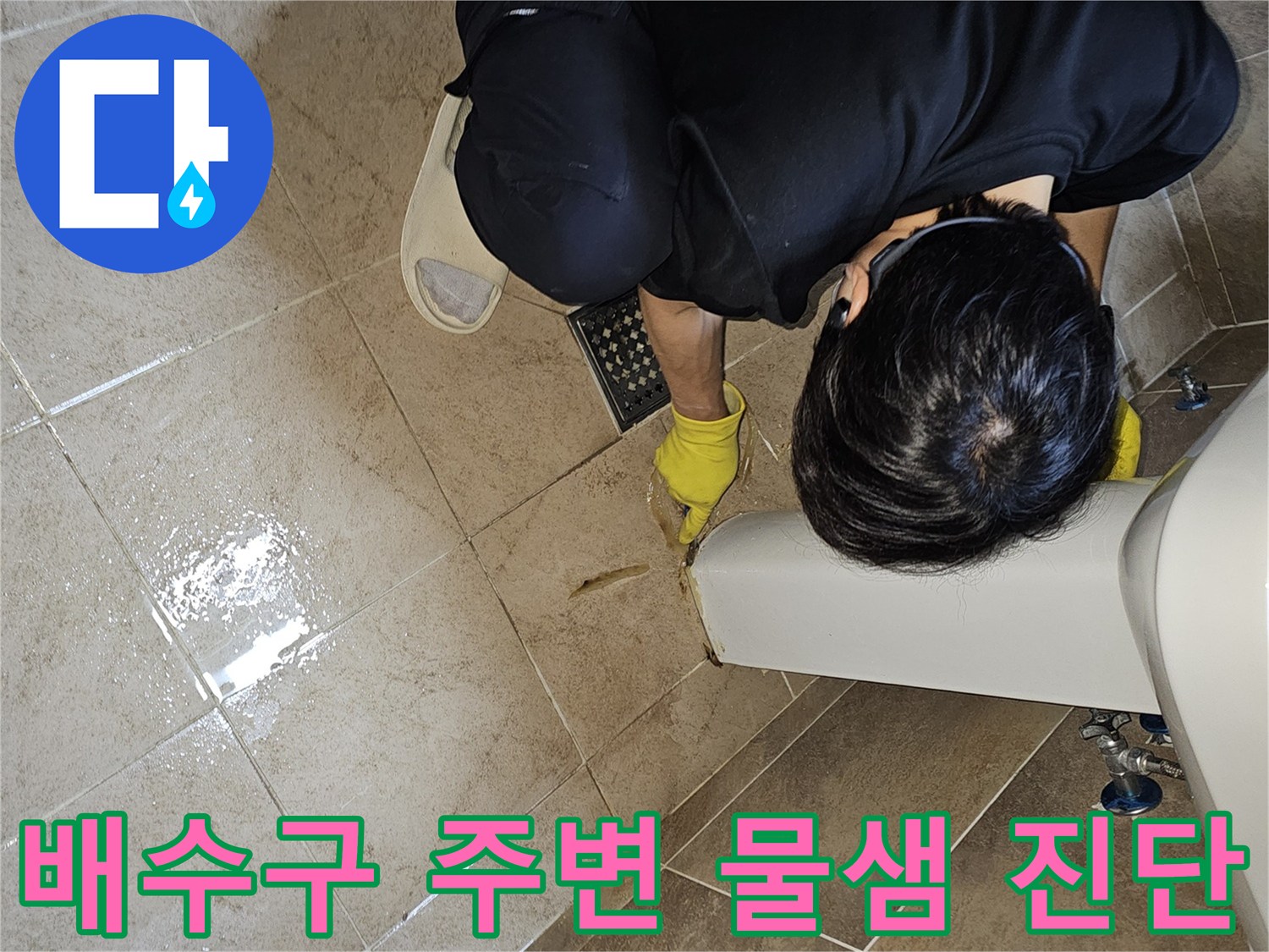 누수 전문가가-노란 장갑을 끼고-욕실 바닥 배수구 주변의-젖은 타일과-틈새를 집중적으로 관찰하며-누수 지점을 파악하고 있습니다