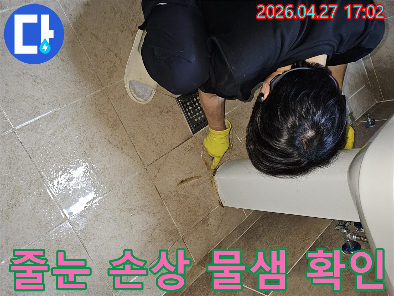 전문 엔지니어가-노란 장갑을 끼고-욕실 바닥 타일의 젖은 줄눈과-그 주변을-손가락으로 가리키며-누수 지점을 면밀히 확인하는 장면