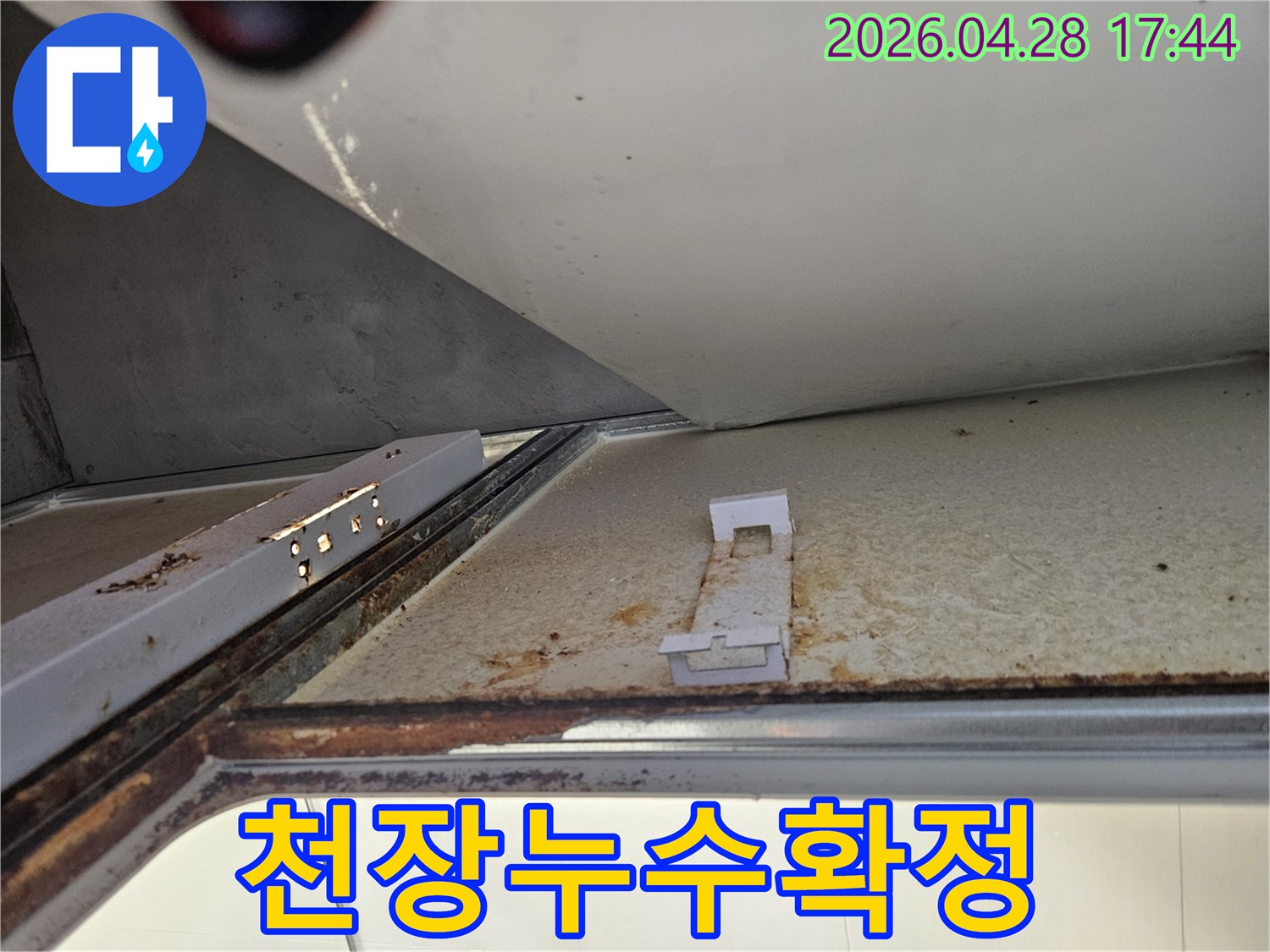 아래층 욕실 천장에서 발견된 심각한 누수 흔적을 보여주는 사진입니다-녹슨 금속 구조물과 변색된 천장 마감재가 명확하게 보입니다.