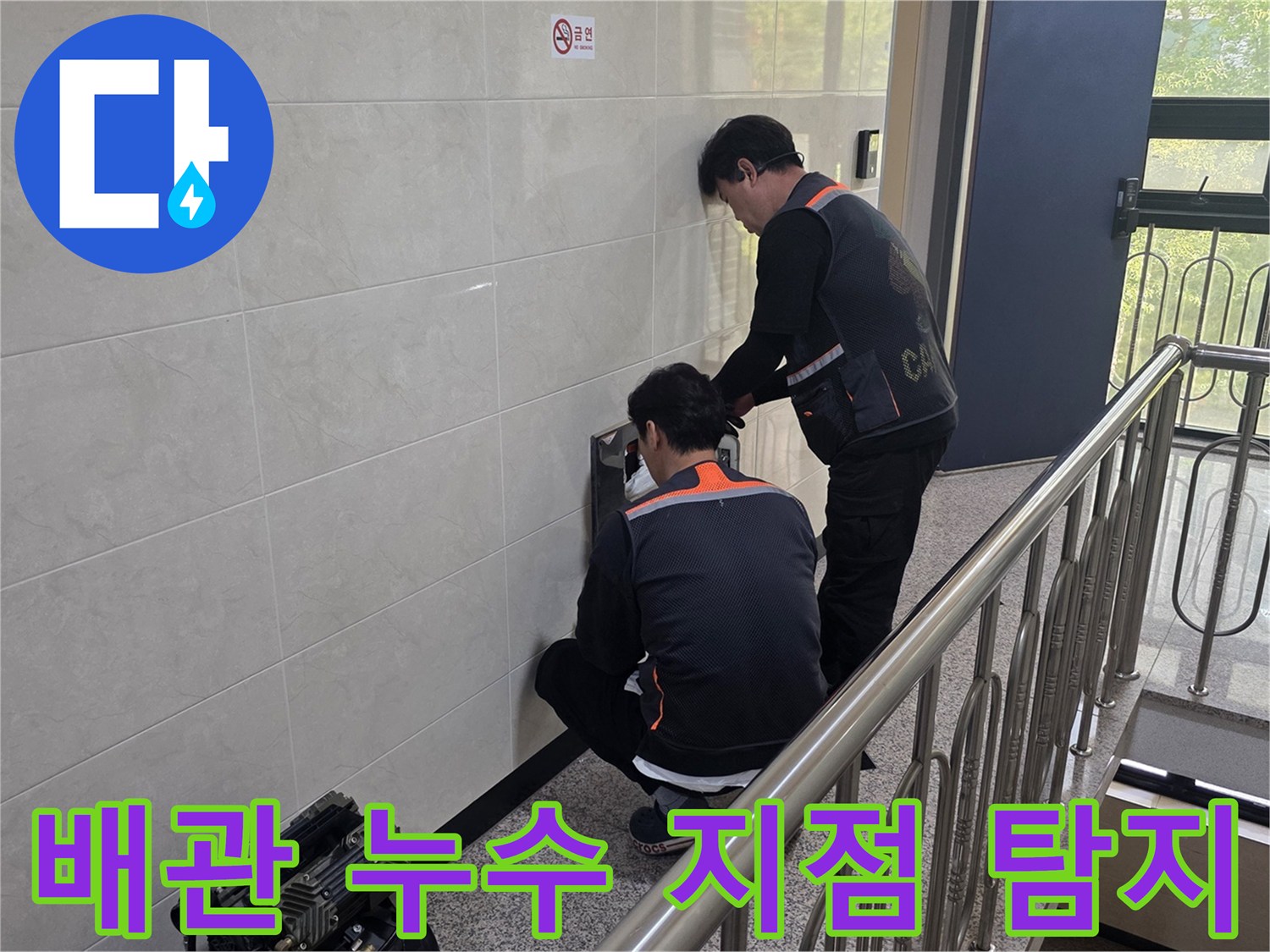 두 명의 전문 기술자가 건물 벽면 내부의 배관 누수 의심 지점을 첨단 장비로 정밀하게 탐지하고 있습니다-정확한 원인 파악을 위한 집중적인 작업입니다.