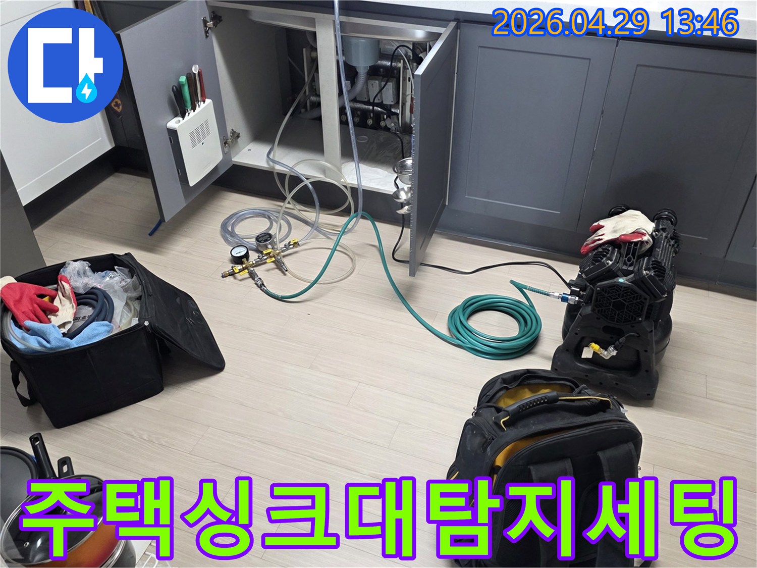동안구 주택의 주방 싱크대 하부에서-누수 탐지를 위한-압력 게이지와 호스-그리고 공기 압축 장비를-설치하는 작업이 진행 중입니다