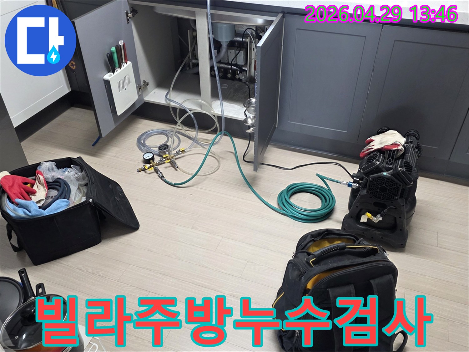 빌라 주방 싱크대 하부에서-배관 누수를 확인하기 위해-압력 게이지와 호스-그리고 공기 압축 장비를-연결하는 작업이 진행 중입니다