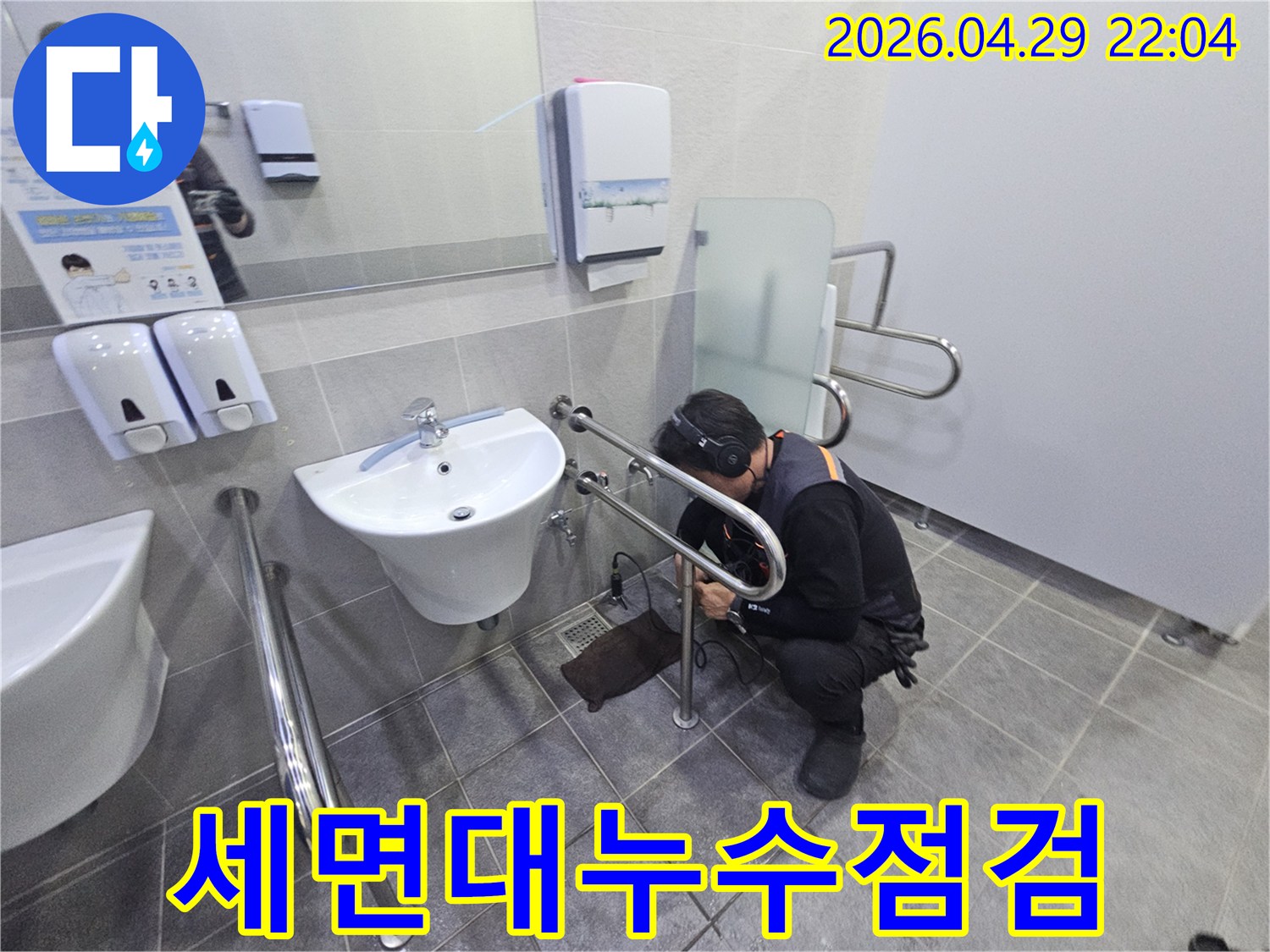 헤드폰을 착용한 기술자가-공용 화장실의 세면대 배관에서-미세한 누수 지점을 찾아내고 있습니다.