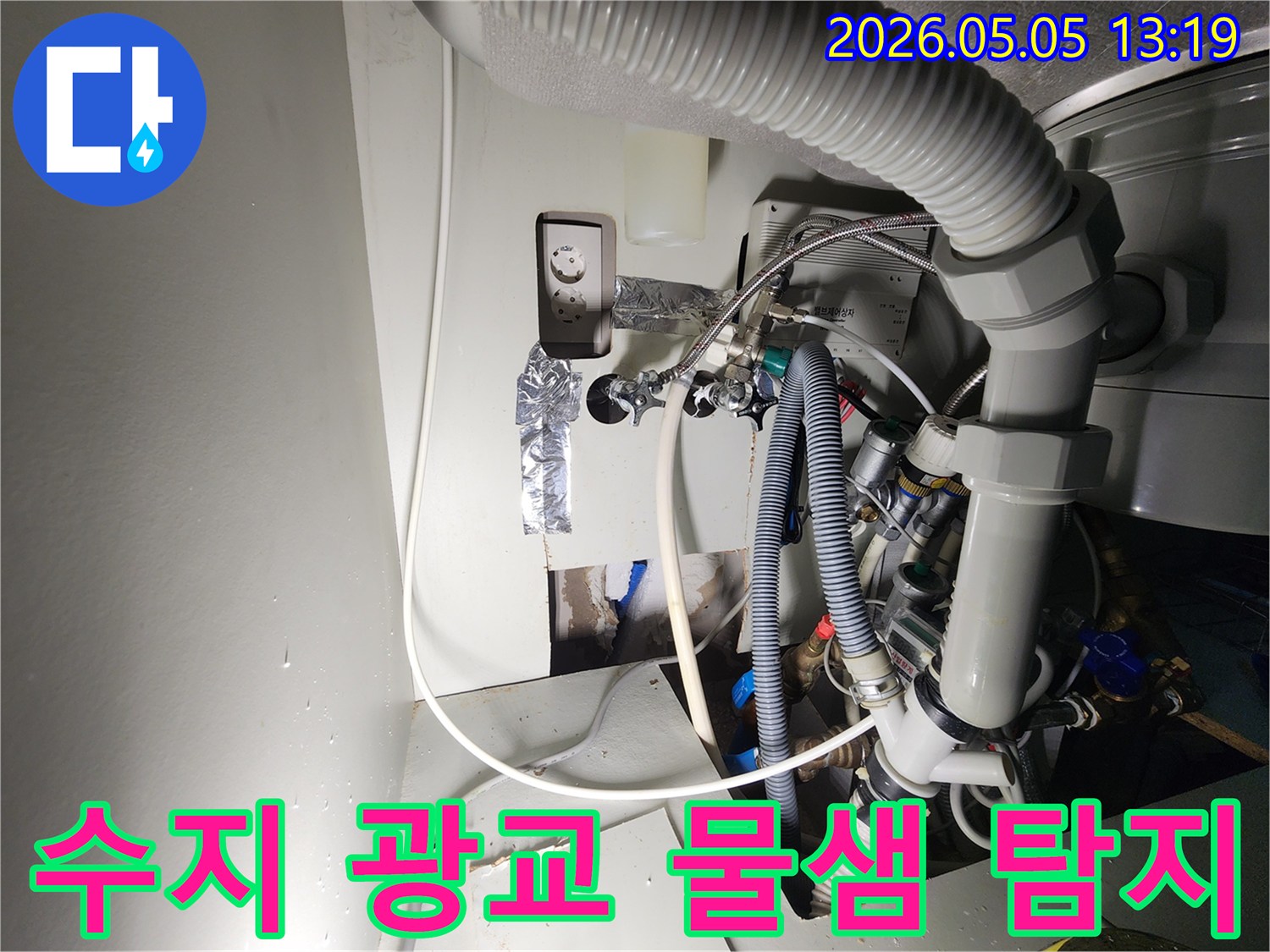 이 이미지는-수지-광교-아파트에서-발생한-물샘-현장을-보여주며-벽면을-개방한-뒤-드러난-복잡한-배관과-전기-시설-사이에서-물이-떨어지는-모습을-촬영한-것입니다