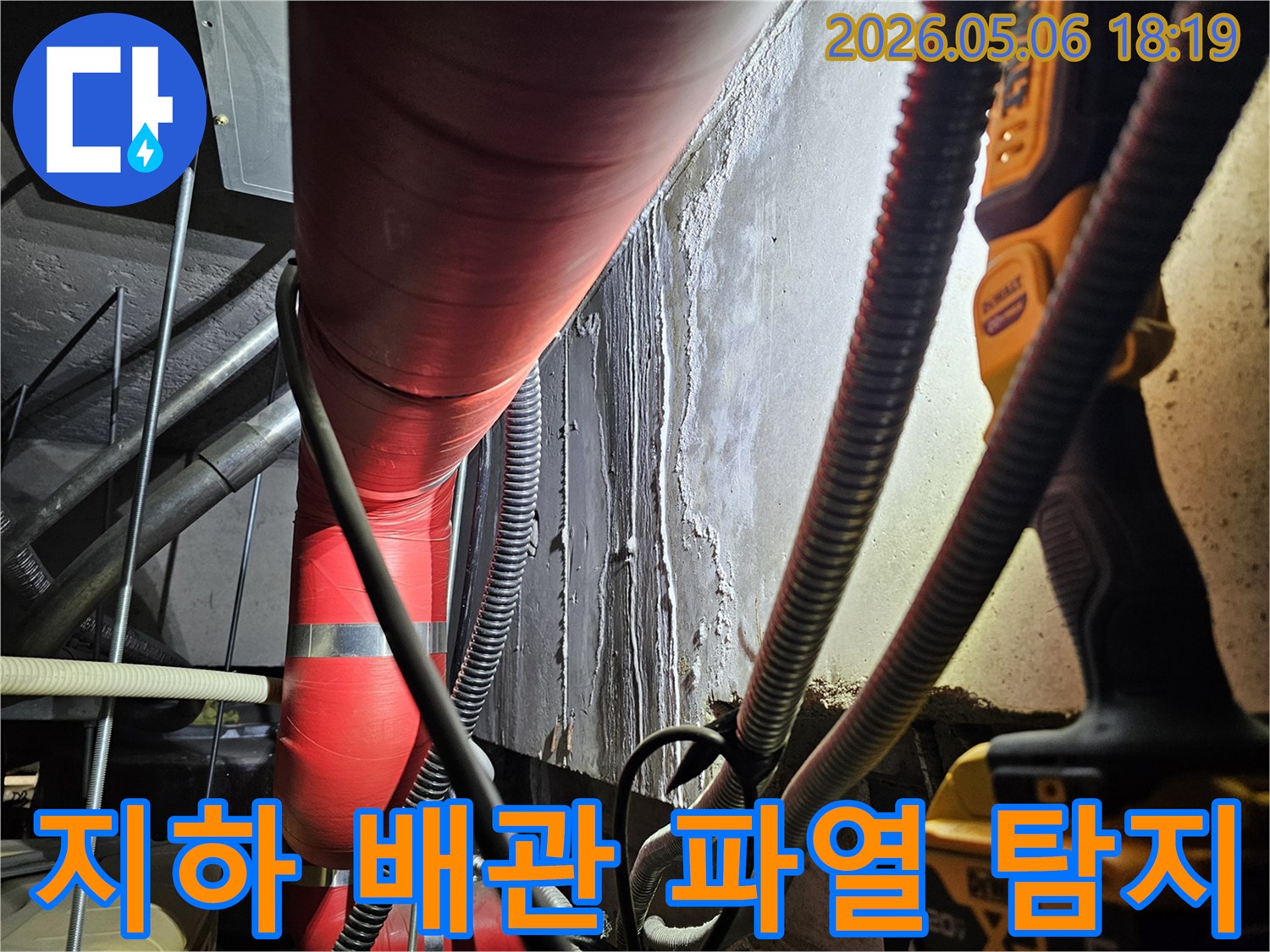 어두운 지하 공간에서-빨간색 단열 배관과-그 주변-젖은 벽면을-전문 탐지 장비로-비추며-배관 파열-여부를-정밀하게-탐지하는-모습
