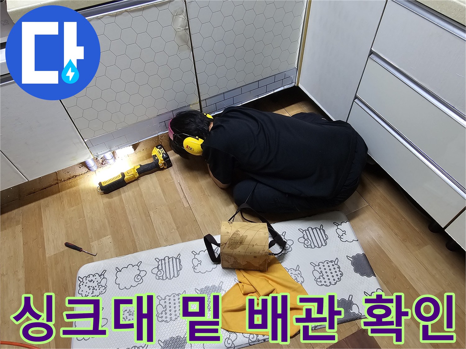 어두운 싱크대 하단-배관 누수 부위를 비추는 조명과 작업자