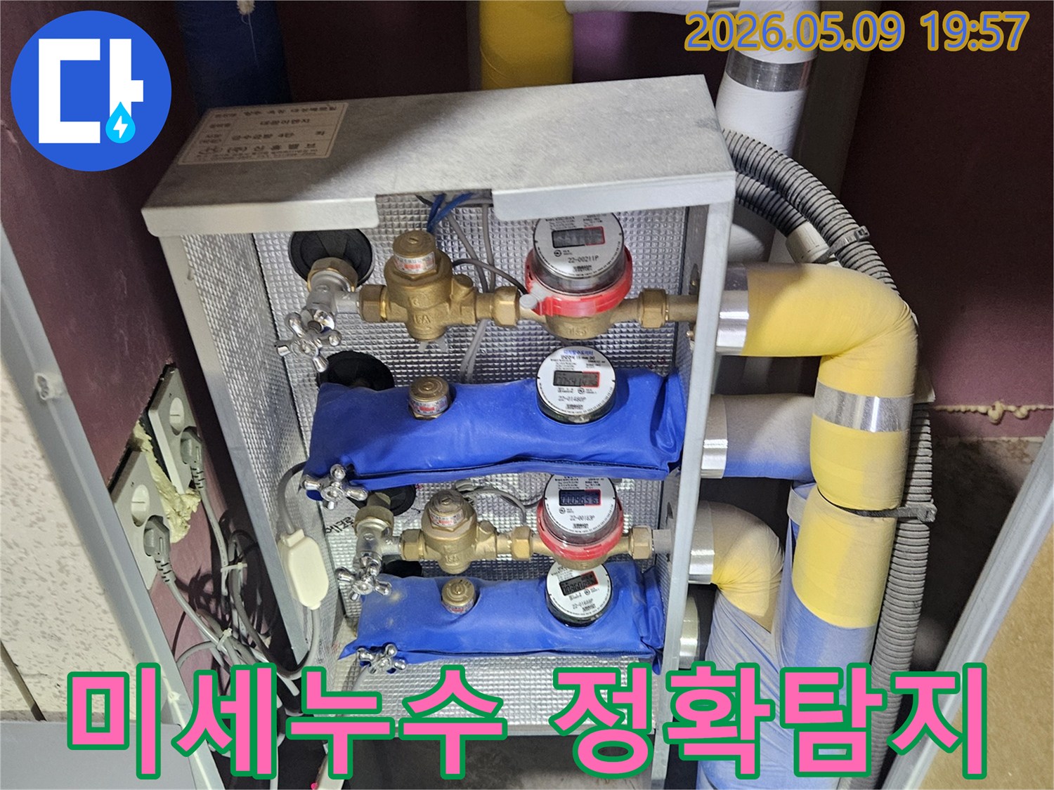 다양한 색상의 단열재로 감싸인 배관과-여러 개의 유량계-밸브가 설치된 난방 분배기 시스템입니다.