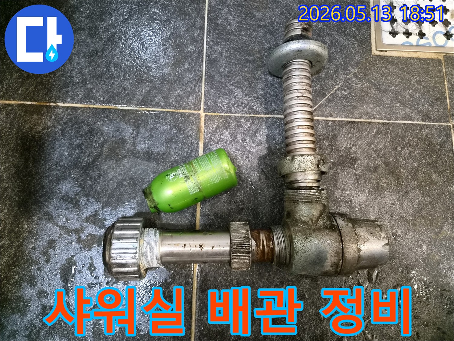 어두운 타일 바닥에-분리된 샤워실 배관 부품과-초록색 샴푸통이 놓여있는-누수 정비 현장 기록
