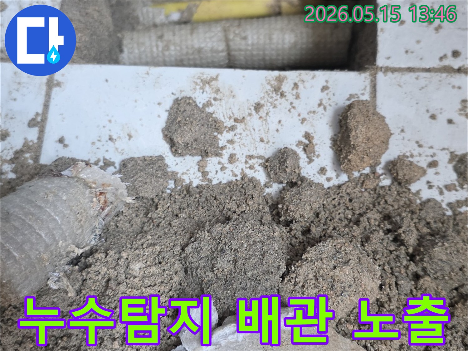 누수 공사 현장에서-바닥을 개방하여-드러난 배관과-주변의 흙더미-그리고-파손된 타일 조각들입니다
