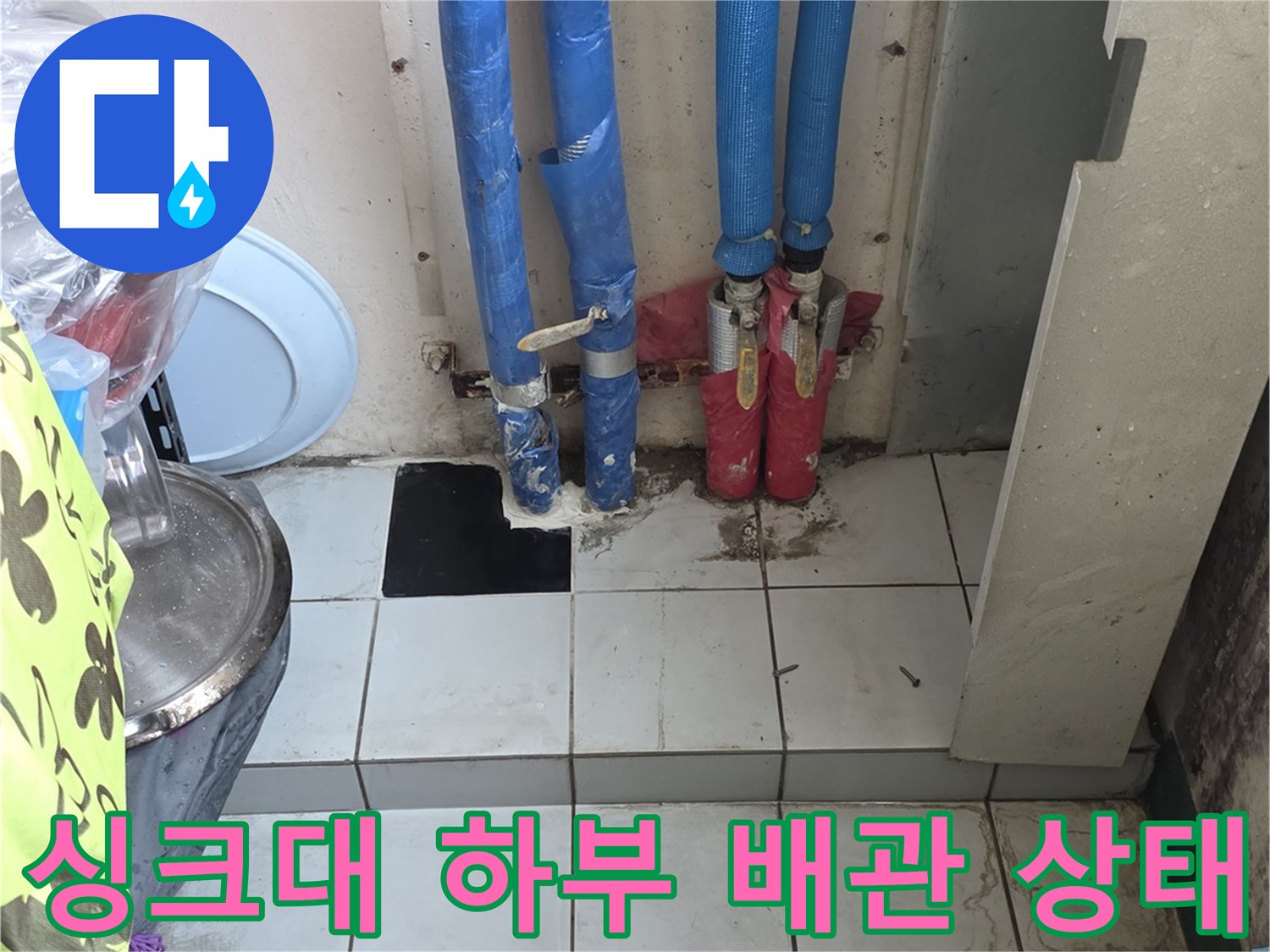 주방 싱크대 하부장 내부의 파란색 보온재로 감싸진 배관 연결 부위 모습입니다.