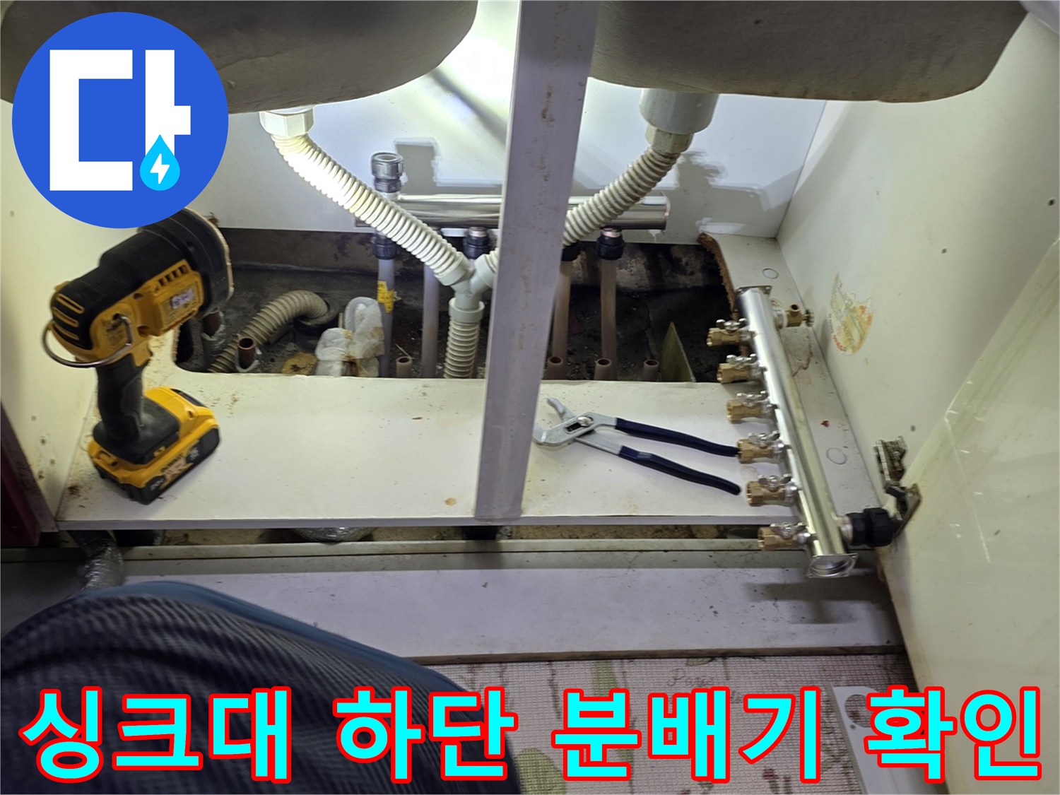 하부장 내부에 노출된 보일러 분배기와 연결 호스들을 점검하는 현장 모습입니다