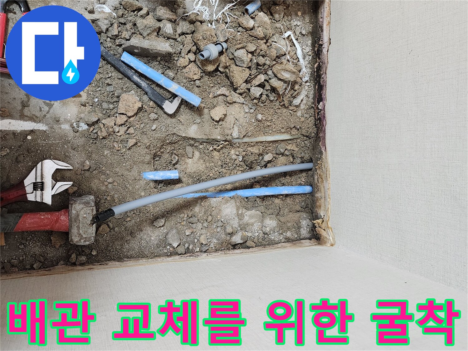 바닥 아래 노출된 파란색 배관과 공구류가 놓인 모습
