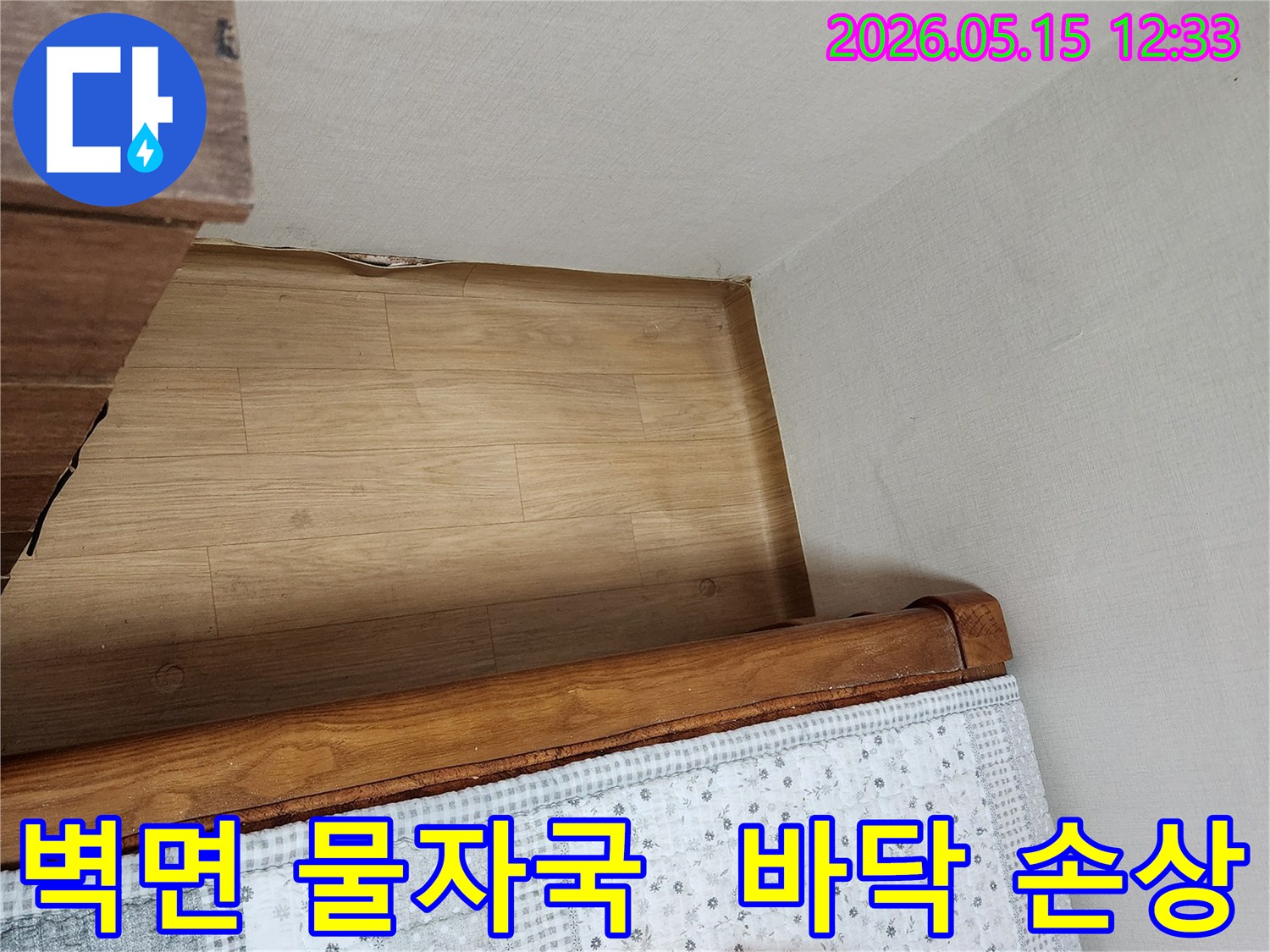 침대-옆-벽면에-선명하게-남은-물자국과-바닥-마루의-손상-징후를-보여주는-사진입니다