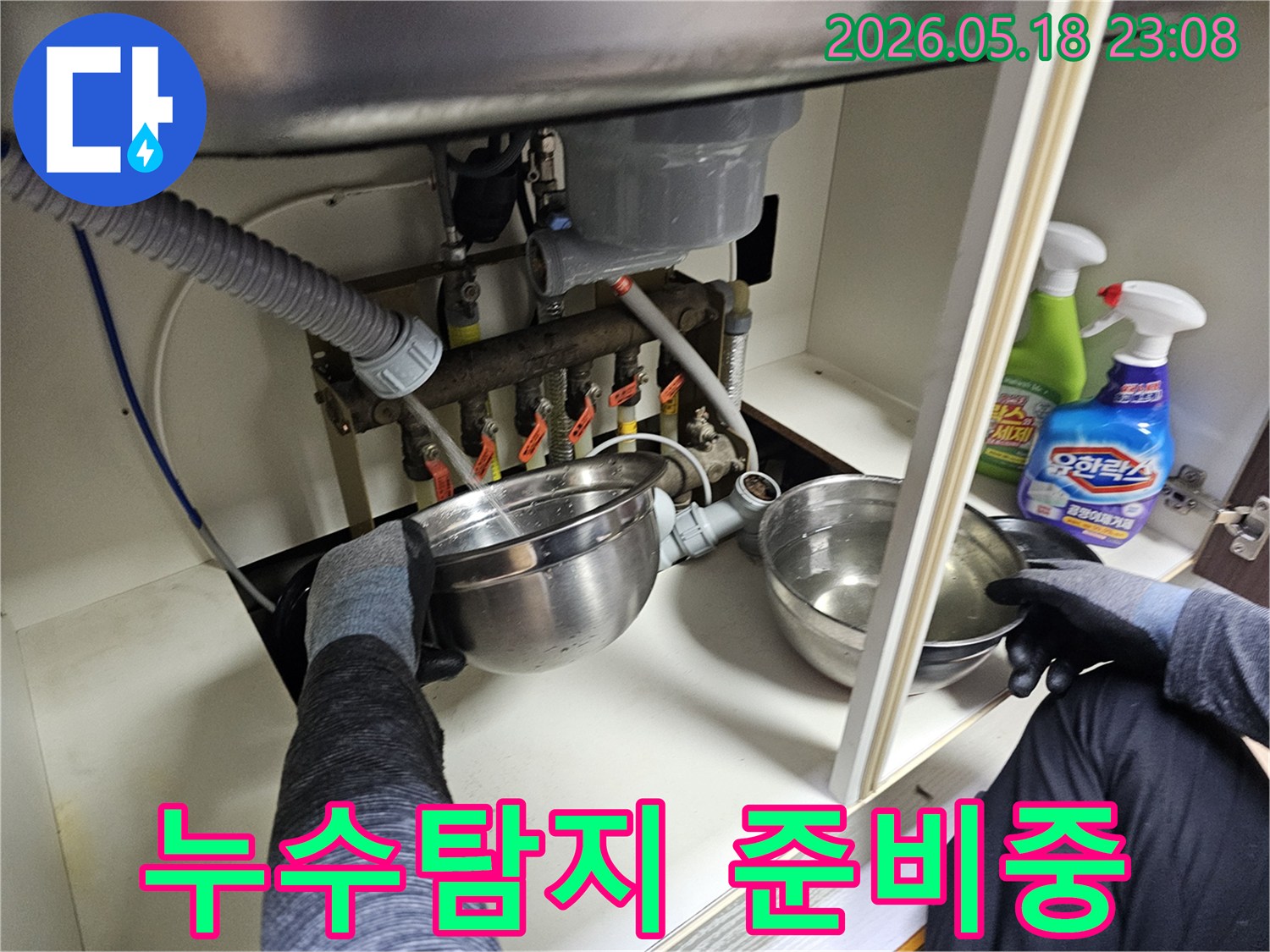 싱크대-하부-배관에서-새는-물을-그릇으로-받아내며-누수-탐지를-위한-현장-정리-작업