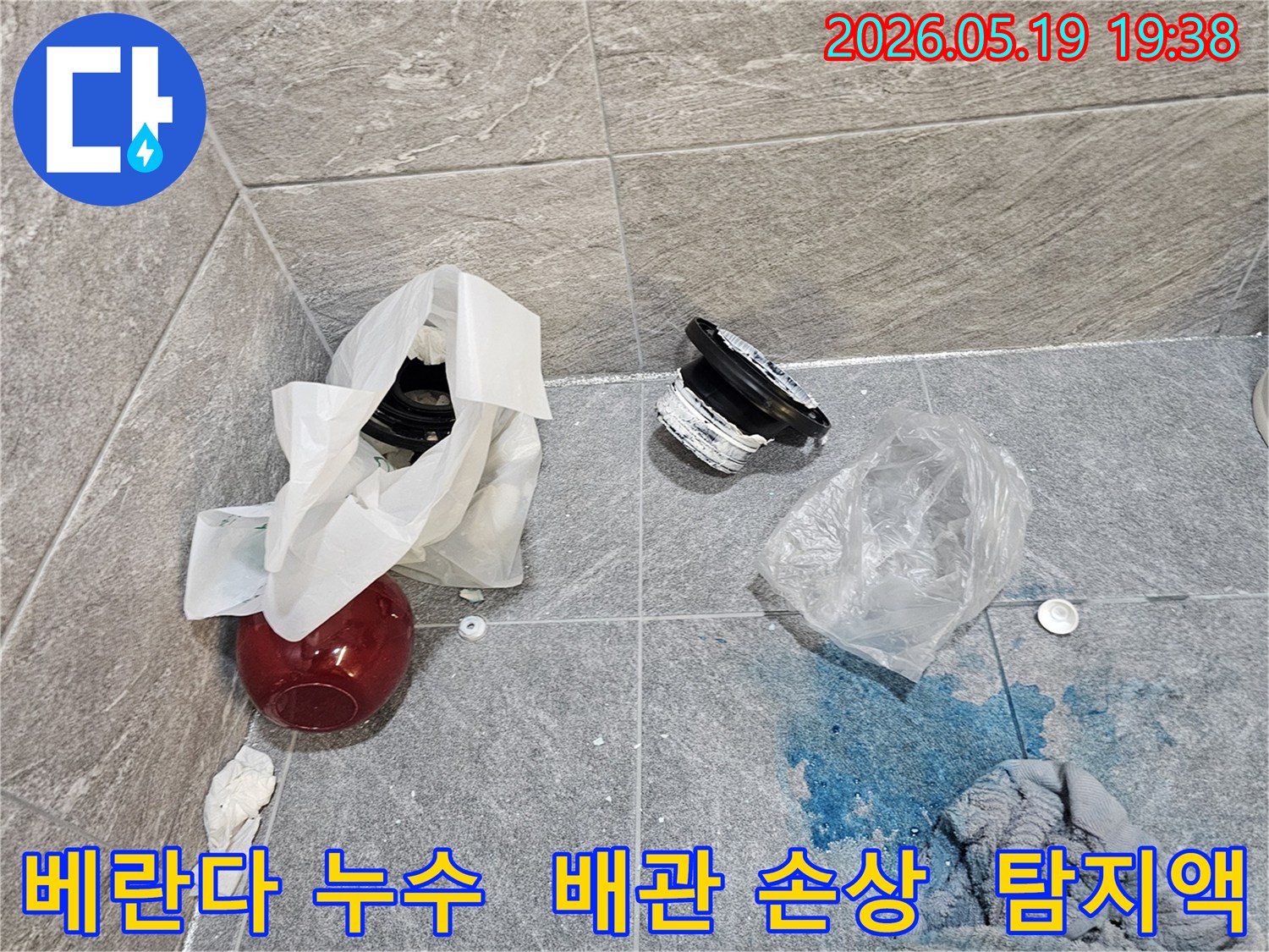 베란다 누수 탐지 현장에서-파란색 탐지액이 바닥에 퍼져 있고-손상된 배관 부품들이 놓여 있는 모습입니다