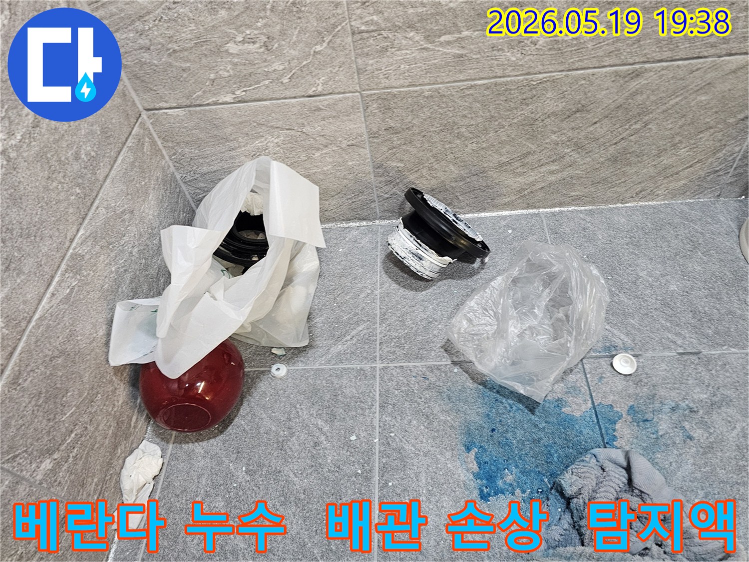 베란다 누수 탐지 현장에서-파란색 탐지액이 바닥에 퍼져 있고-손상된 배관 부품들이 놓여 있는 모습입니다