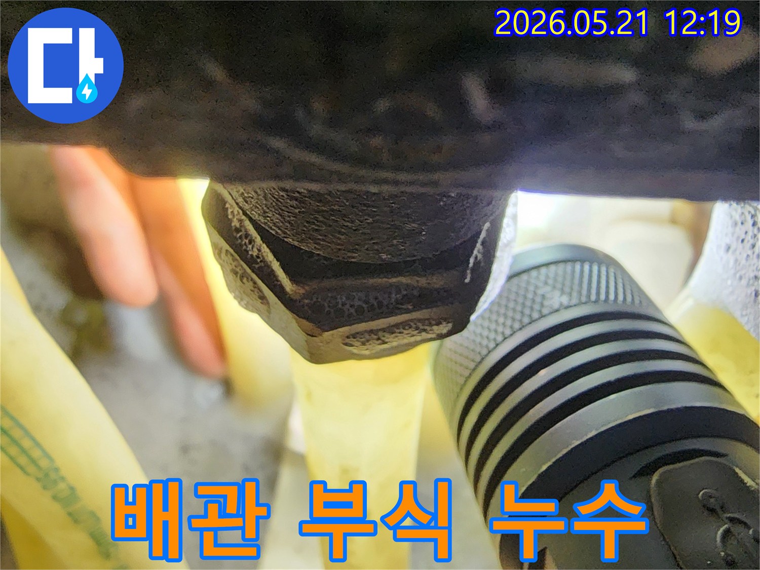 플래시 빛 아래-오래된 배관의-부식된 연결 부위에서-발생한 누수 흔적을-면밀히 관찰하는 장면