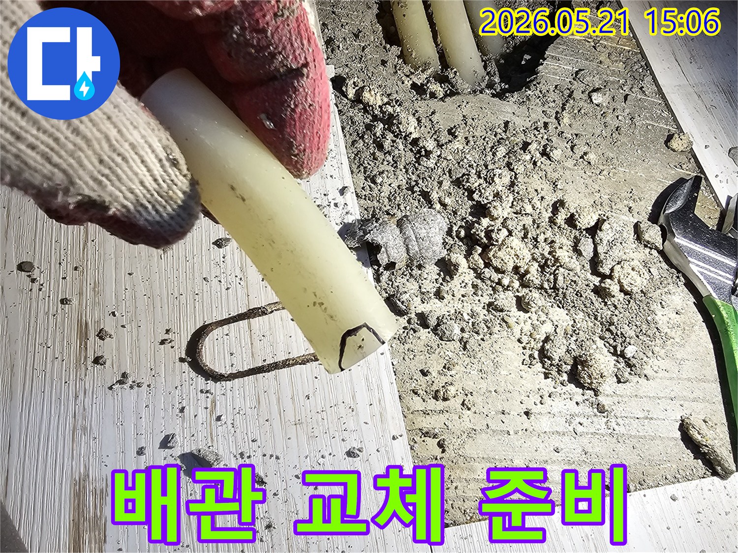 작업 장갑을 낀 손이 손상된 배관 조각을 들고-누수 수리 현장을 보여주는-사진입니다