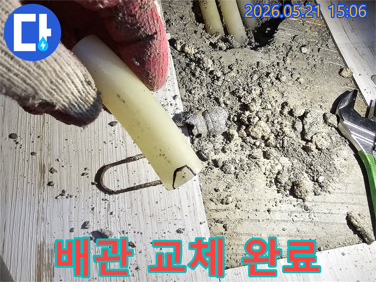 작업 장갑을 낀 손이 파손된 배관 조각을 들고-교체 완료를 설명하는-현장 사진입니다