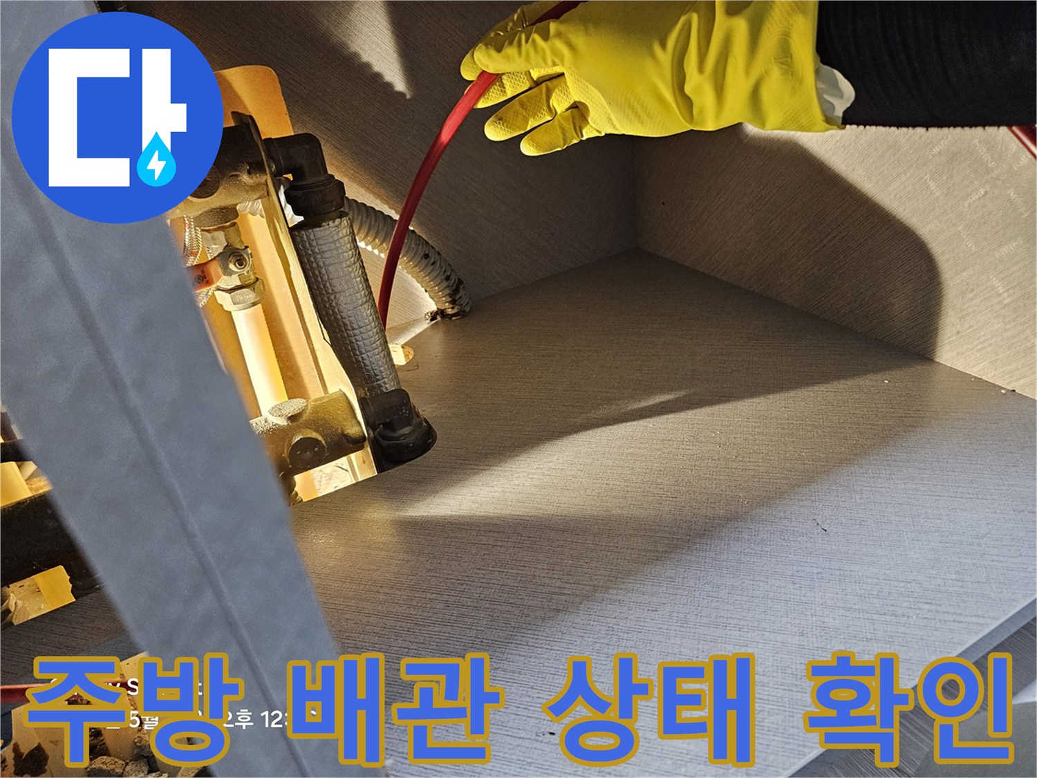 작업자가 노란 장갑을 끼고 싱크대 하부의 금속 배관을 만져보며 점검합니다.