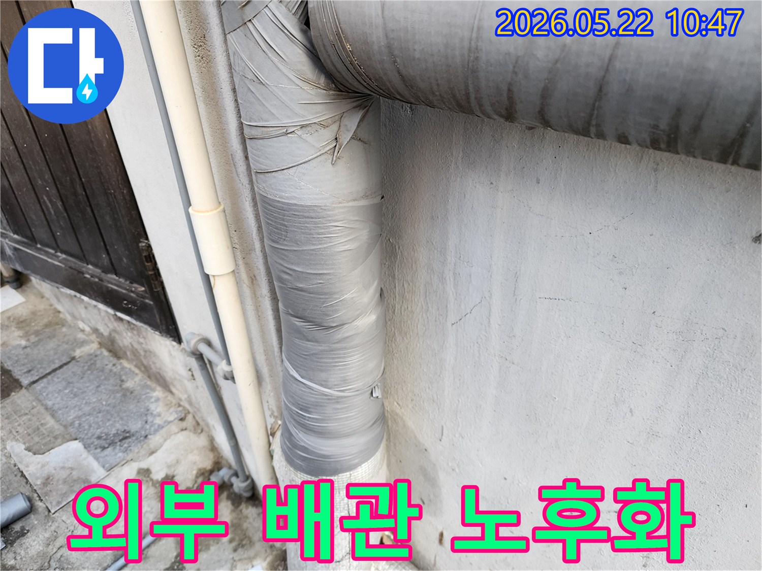 건물-외벽에-설치된-회색-배관의-보온재가-낡은-테이프로-감겨-있으며-전반적인-노후화가-진행된-모습입니다