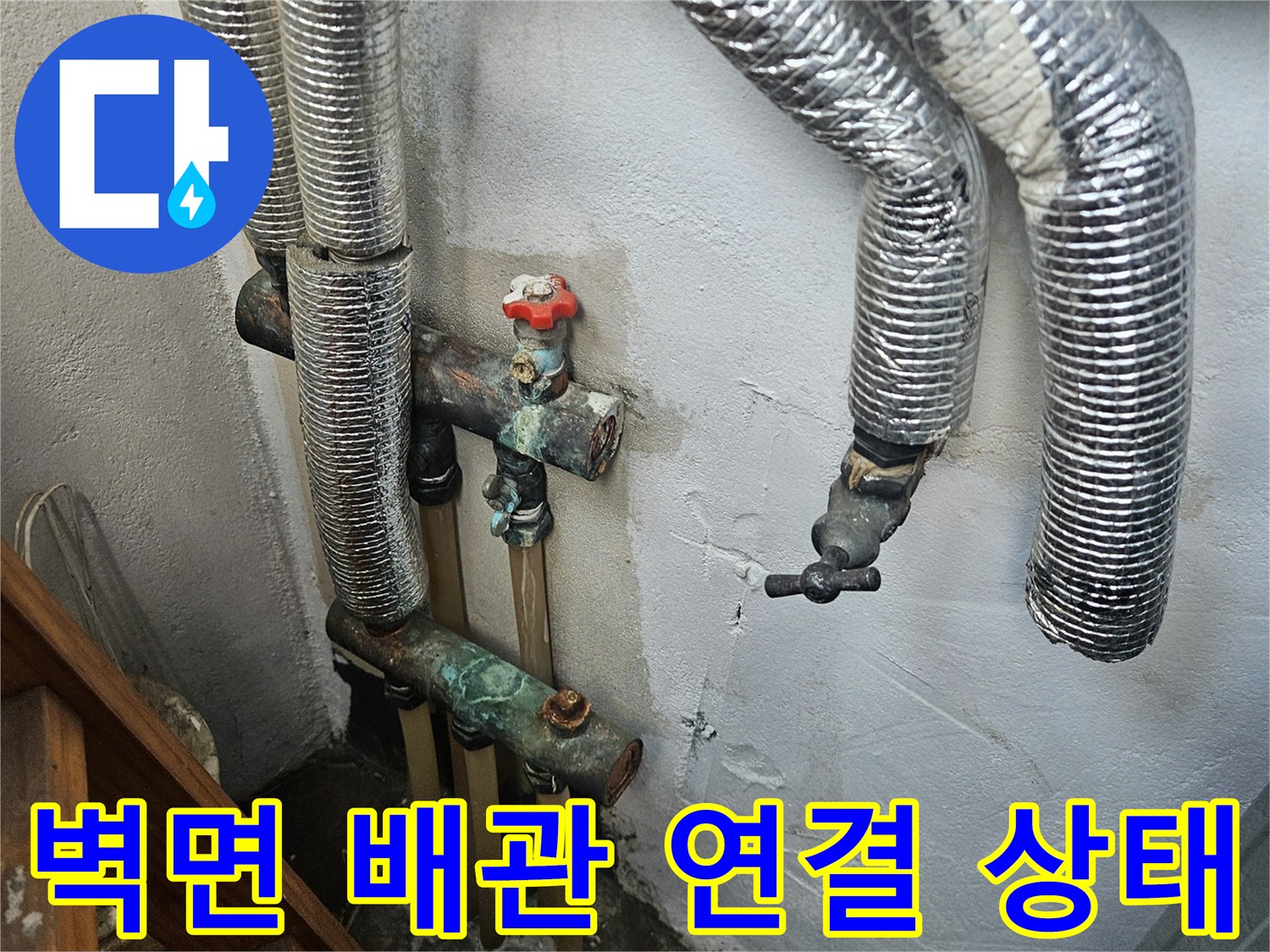 벽면에 노출된 은색 보온재 배관과 금속 부속의 모습입니다.