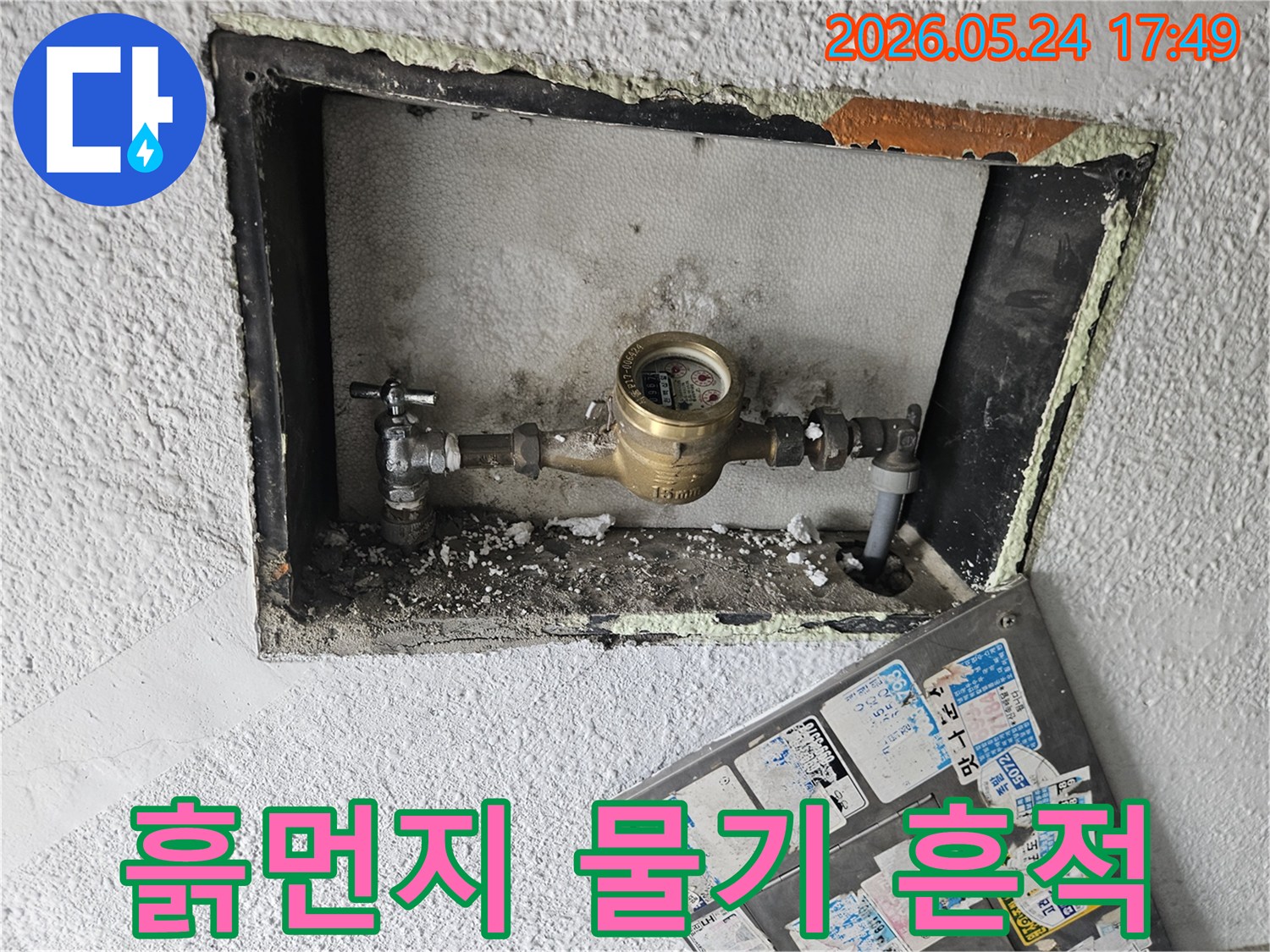 수도 계량기 주변에 쌓인 흙먼지와-물기로 인한 얼룩이-누수를 암시하는 이미지입니다.