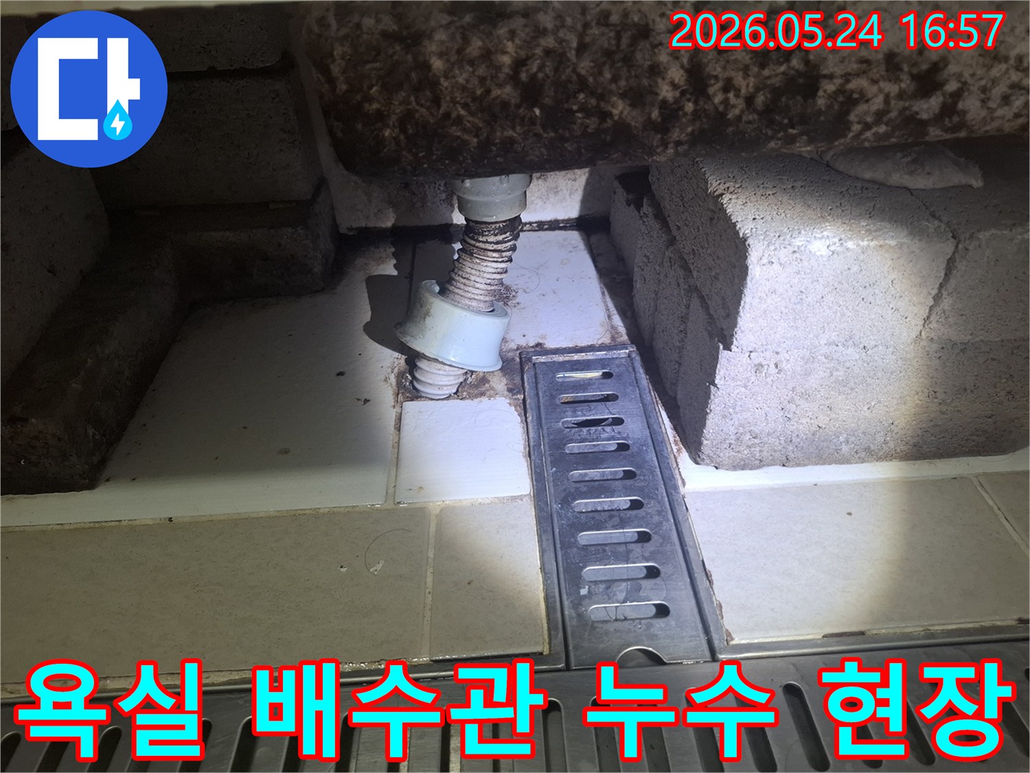 이 이미지는 광명 아파트 욕실 바닥 배수구와 연결된 낡은 배수관 주변의 누수 흔적을 보여줍니다-전문가가 정밀 진단을 위해 현장을 점검하고 있습니다.