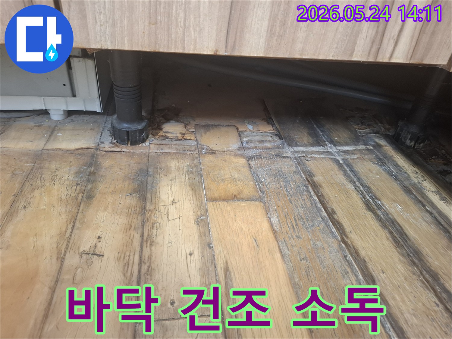 물에 젖어 어둡게 변색되고 부식된 나무 바닥과-그 옆에 위치한 검은색 배관이 보입니다