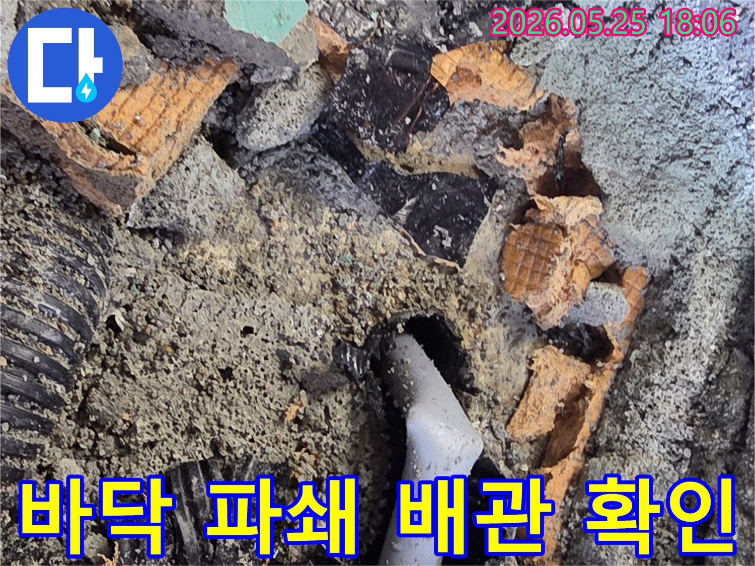파쇄된 바닥 아래로 드러난 젖은 배관과 주변의 흙-콘크리트 조각들은-누수 수리를 위한 배관 교체 작업을 보여줍니다.