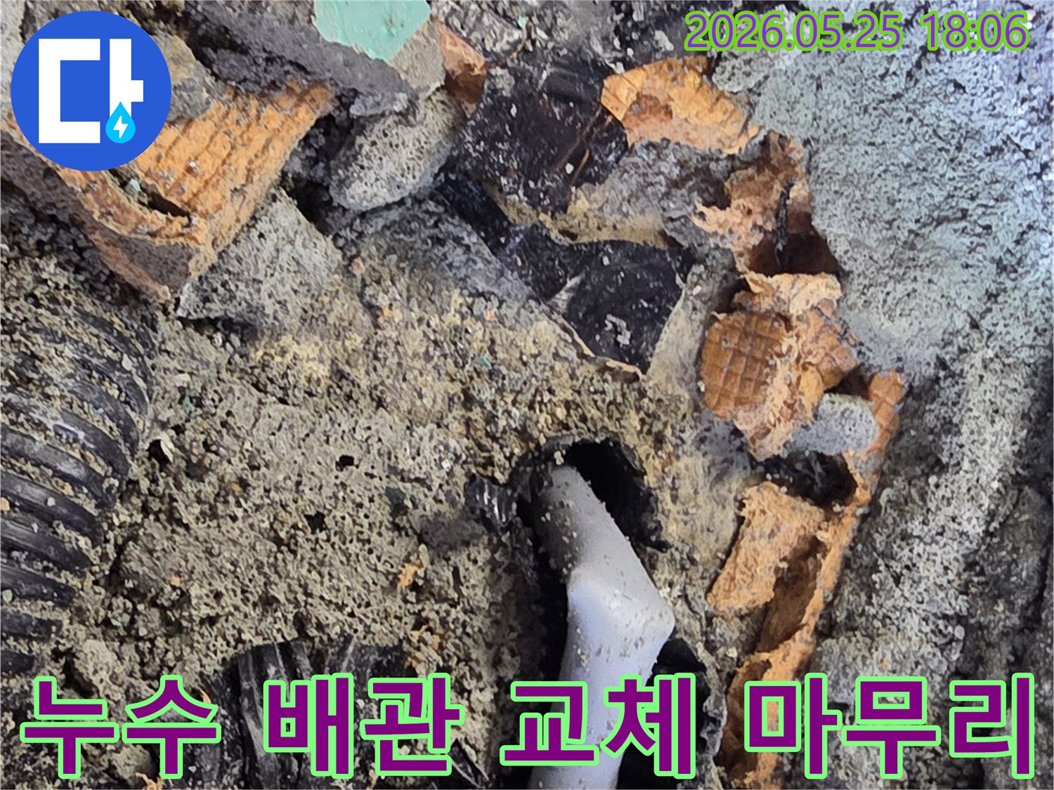 파쇄된 바닥 아래에서 발견된 젖은 배관과 주변의 흙-콘크리트 조각들은-누수 수리를 위한 배관 교체 작업을 보여줍니다.